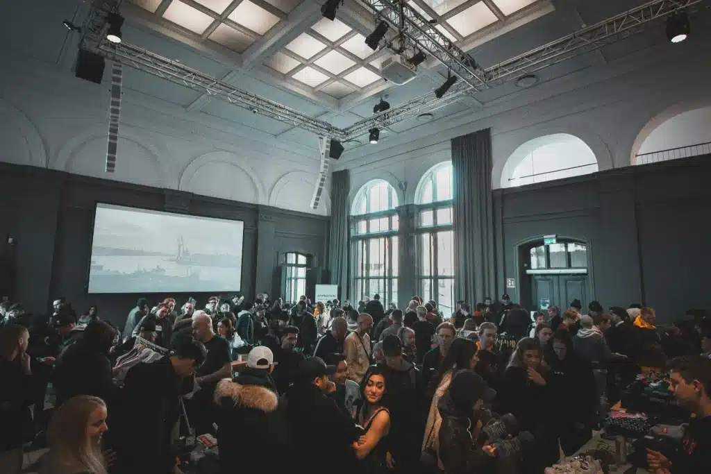 Crowded indoor market event with people browsing tables under bright overhead lighting