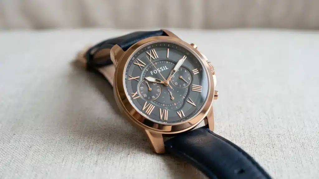 A close-up shot of a Fossil chronograph watch with a navy blue leather strap resting on a textured light beige surface
