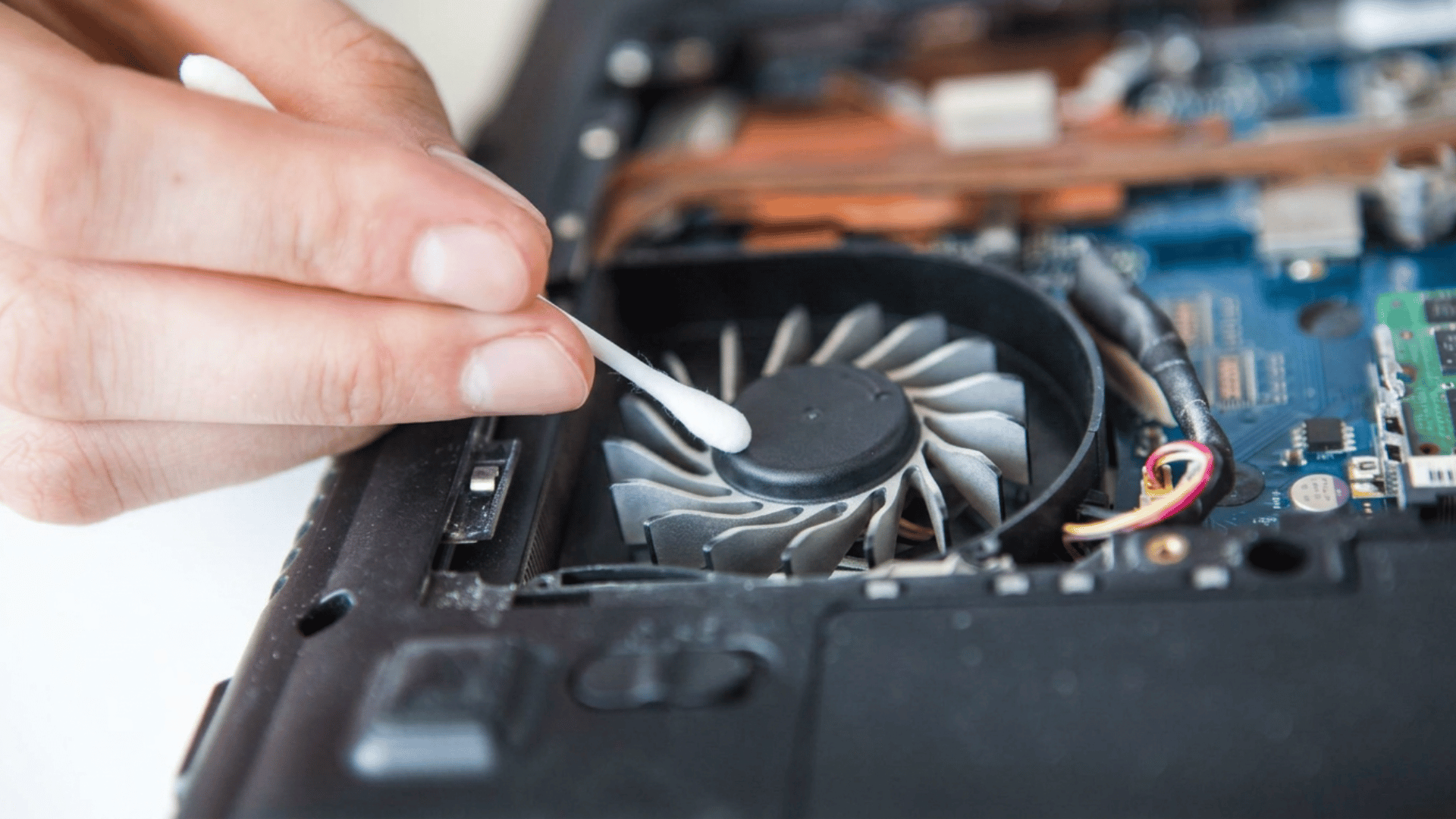A close-up shot shows a hand holding a cotton swab, cleaning a dusty computer fan