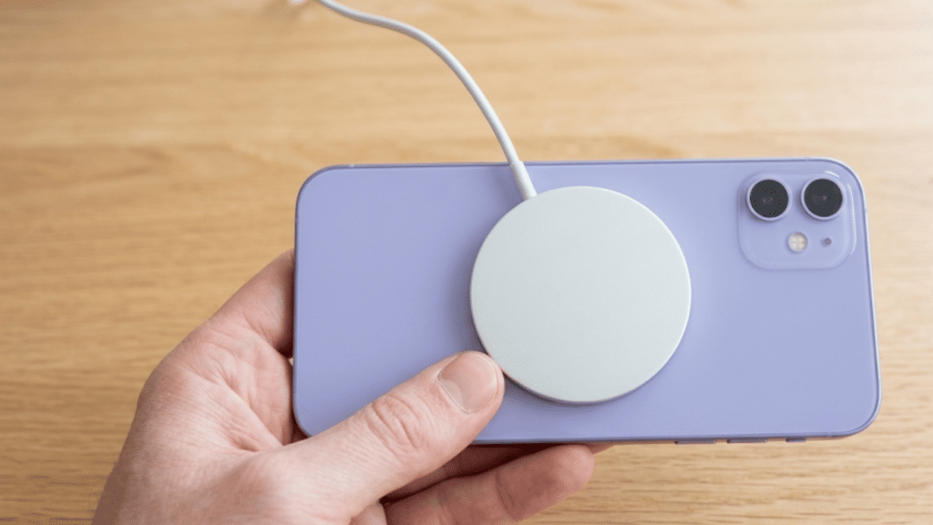 a hand holding a purple iphone with a magnetic wireless charger attached on a wooden table
