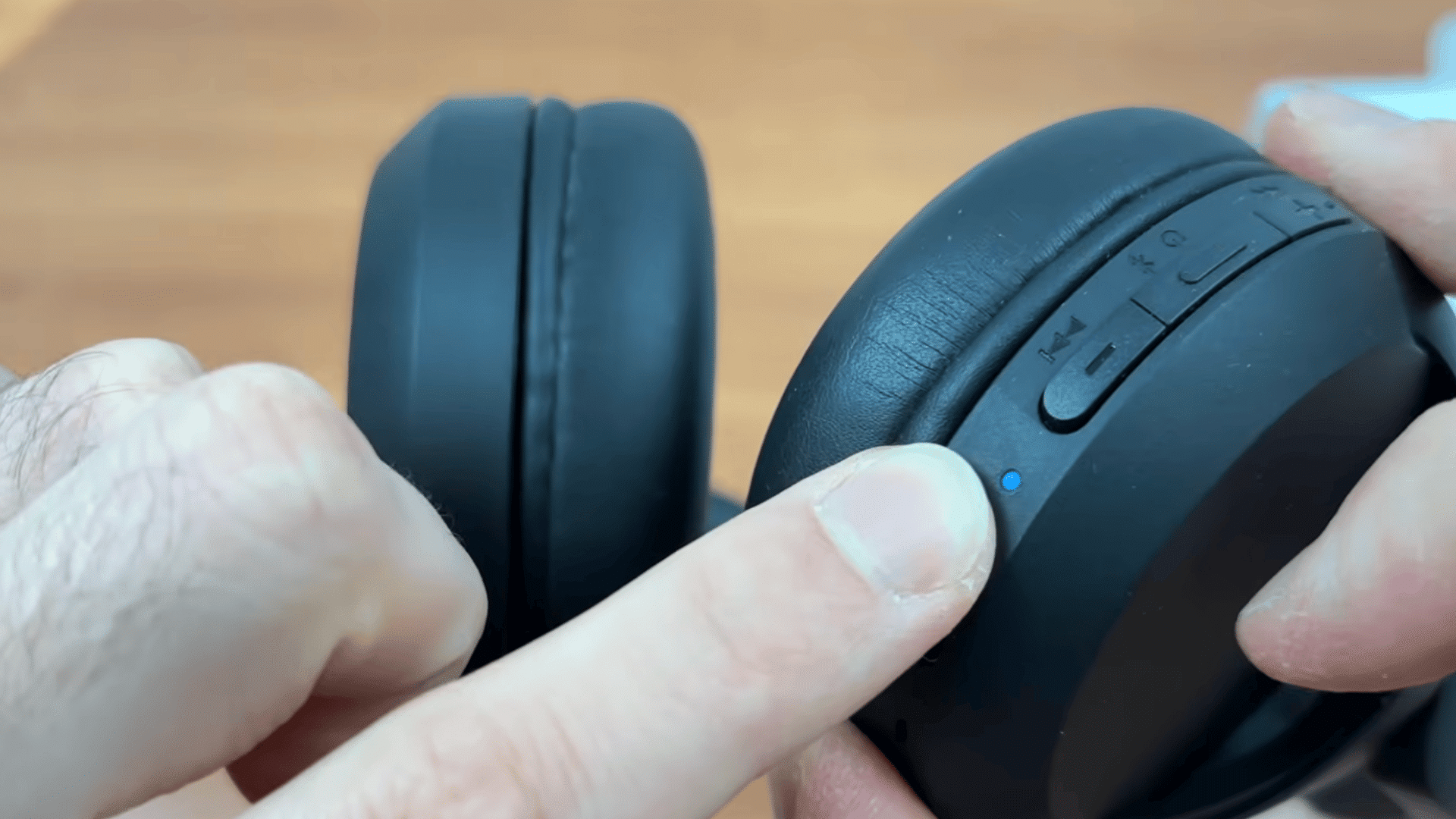 a hand pointing to the blue status light on black over ear headphones during bluetooth pairing setup