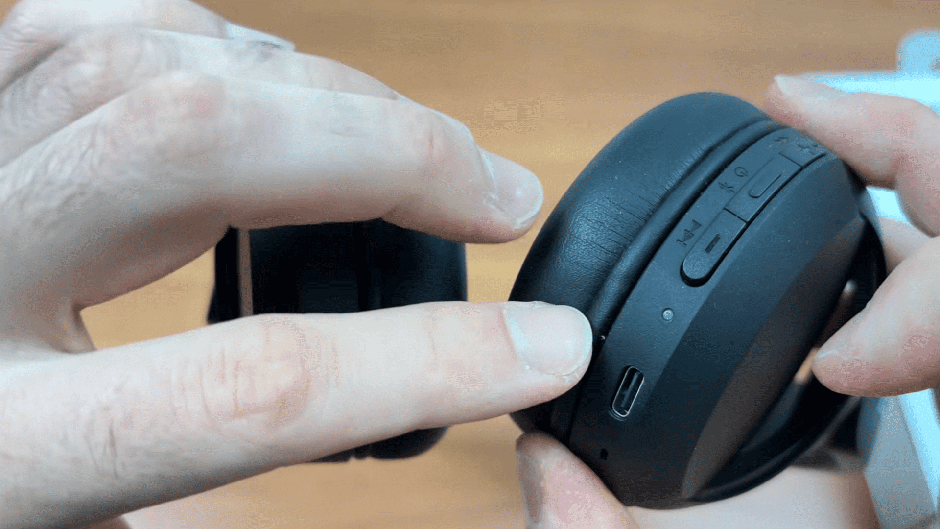 a hand pointing to the power and volume control buttons on black over ear headphones during a setup demonstration