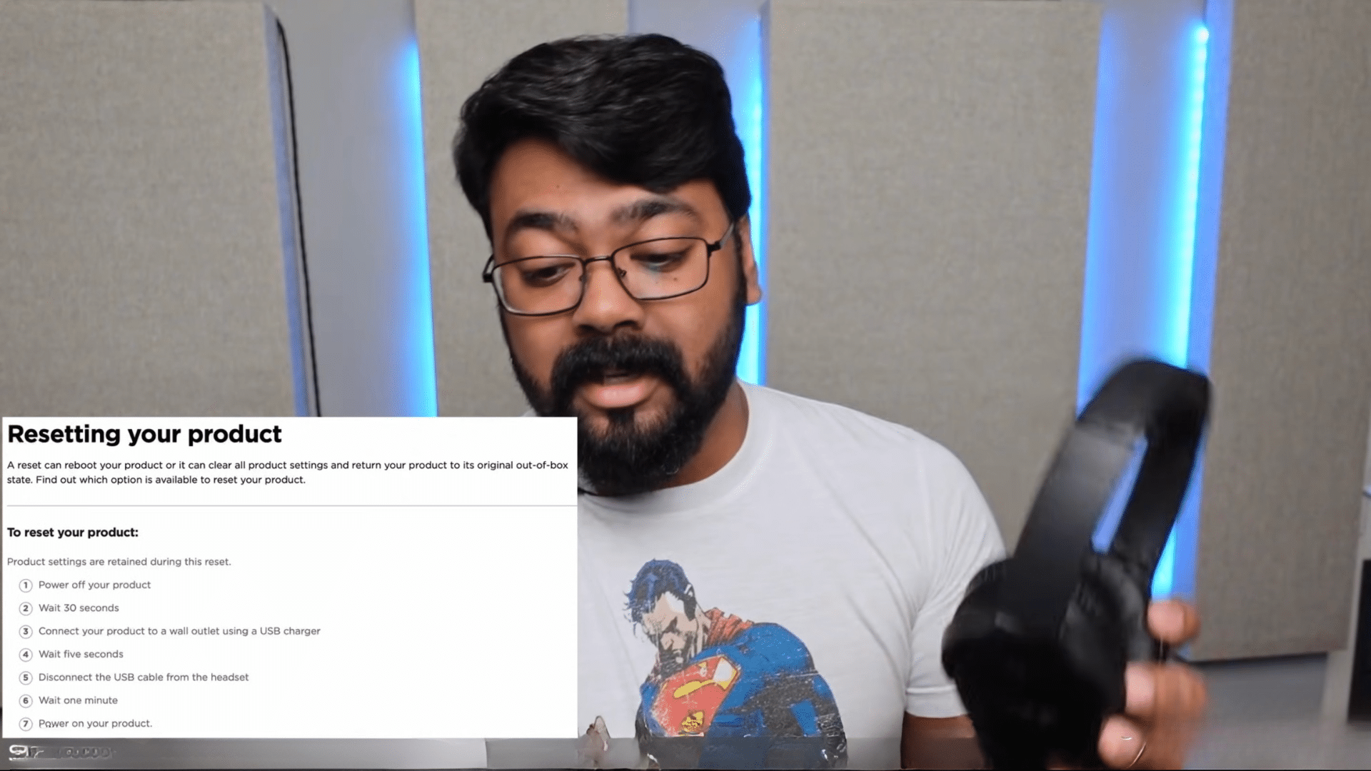 a man wearing glasses and a superman shirt holds black headphones beside reset instructions on a computer screen