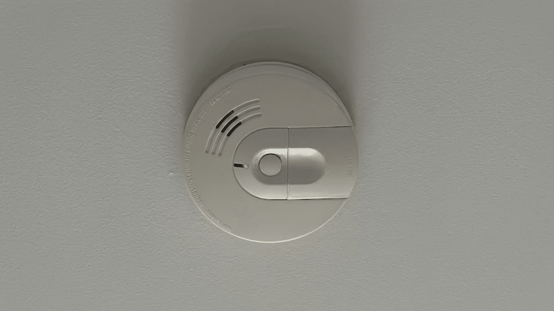 a white smoke detector mounted on a smooth ceiling with a green indicator light showing the device is powered and active