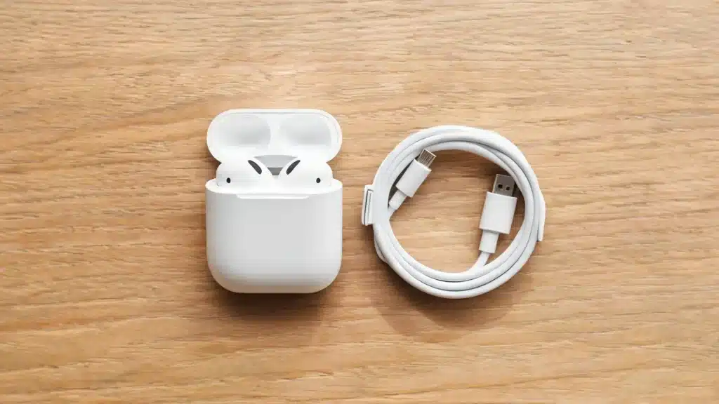AirPods in an open charging case beside a USB-C cable on a wooden table