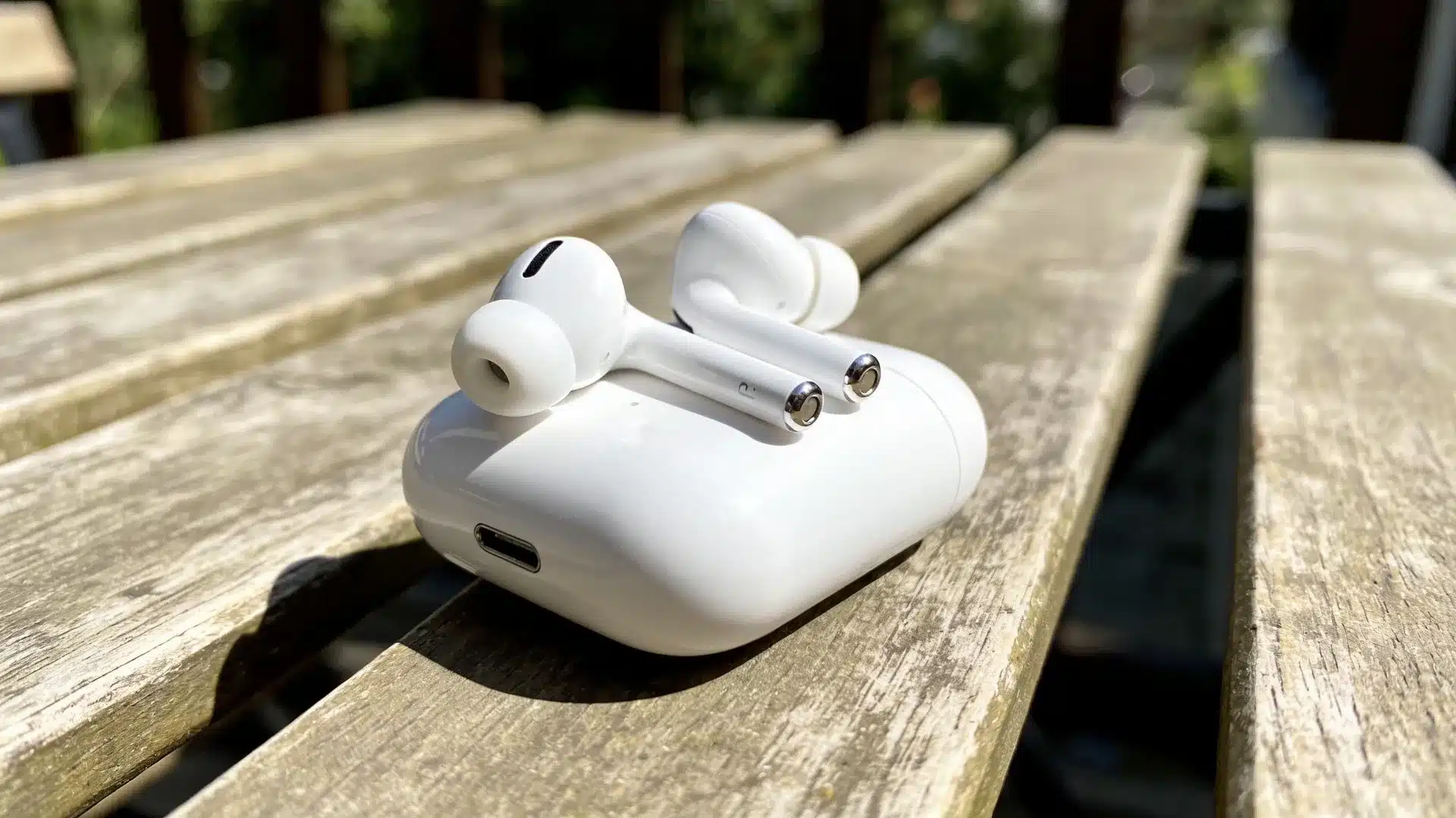 AirPods Pro earbuds resting on a closed charging case on a sunny wooden outdoor table