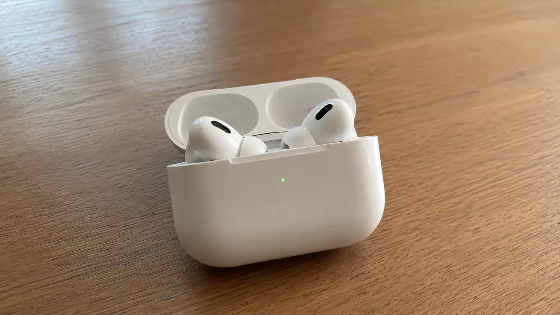 AirPods in an open charging case on a wooden table with green charging light