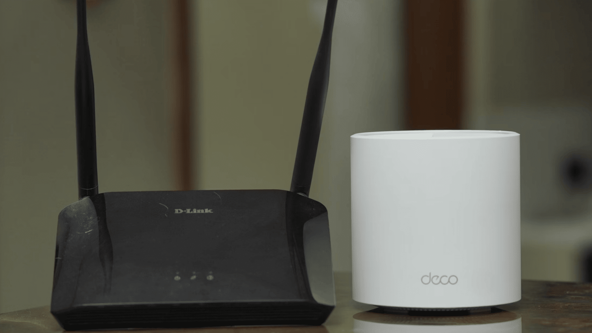 black wireless router beside a white mesh wifi device placed together on a wooden tabletop indoors