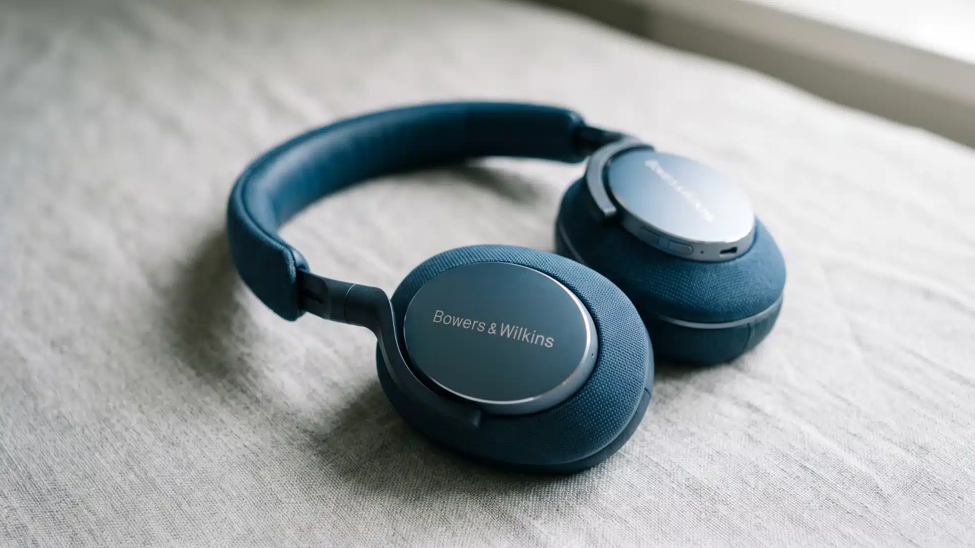Blue Bowers & Wilkins wireless headphones resting on soft gray fabric