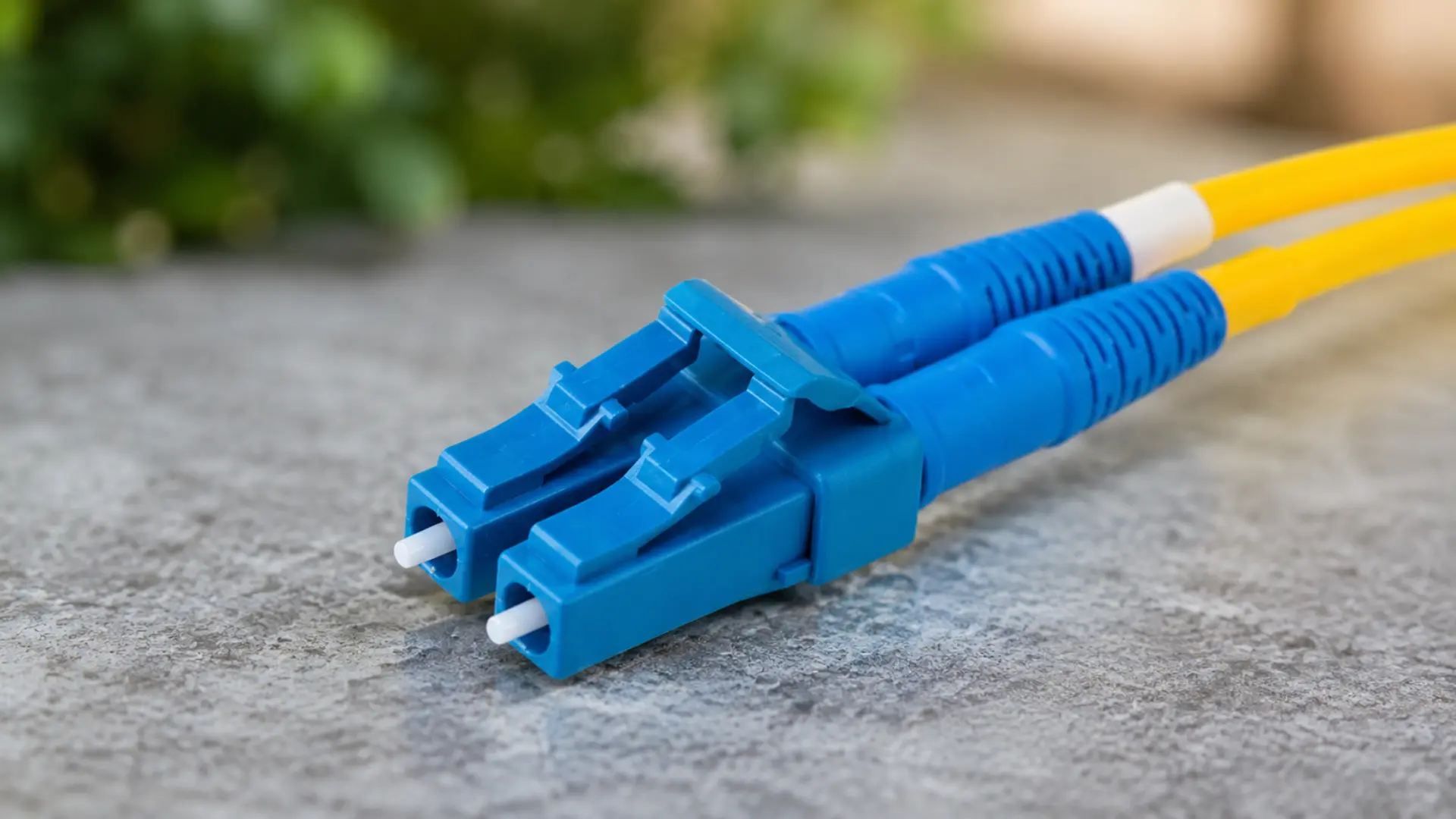 Blue LC fiber optic connector on a gray surface with yellow cables in the background