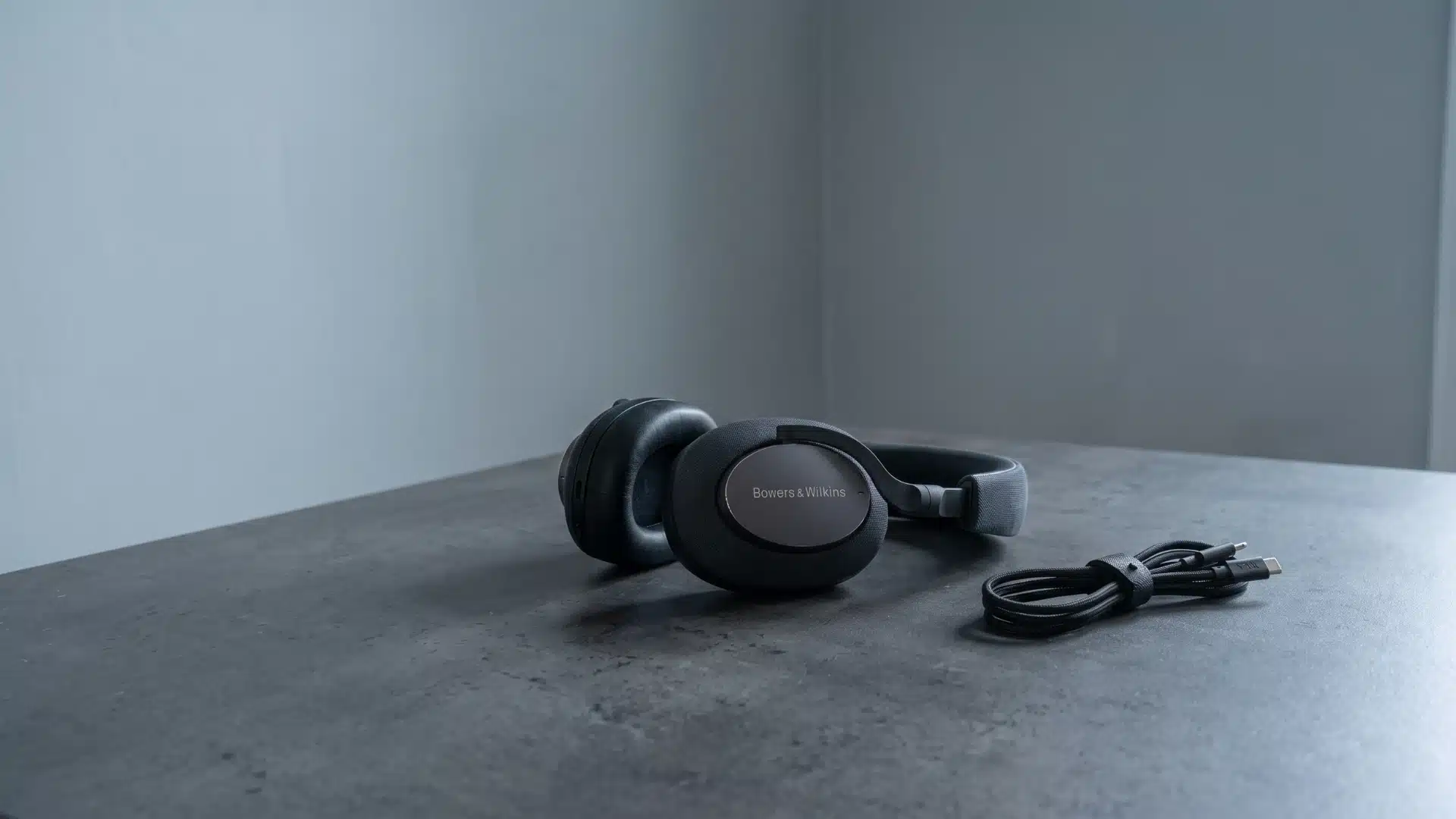 Bowers & Wilkins headphones displayed with a charging cable on a dark table