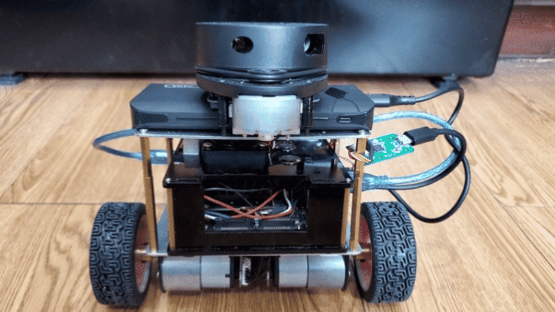 compact mobile robot with lidar sensor stacked electronics and two drive wheels on a wooden floor