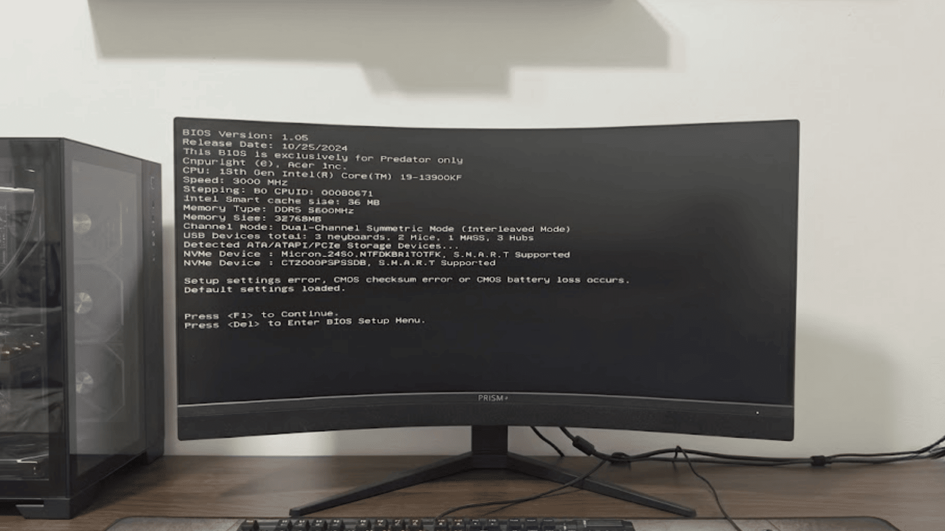 desktop computer with monitor showing bios checksum error message beside a gaming pc keyboard and mouse on a wooden desk