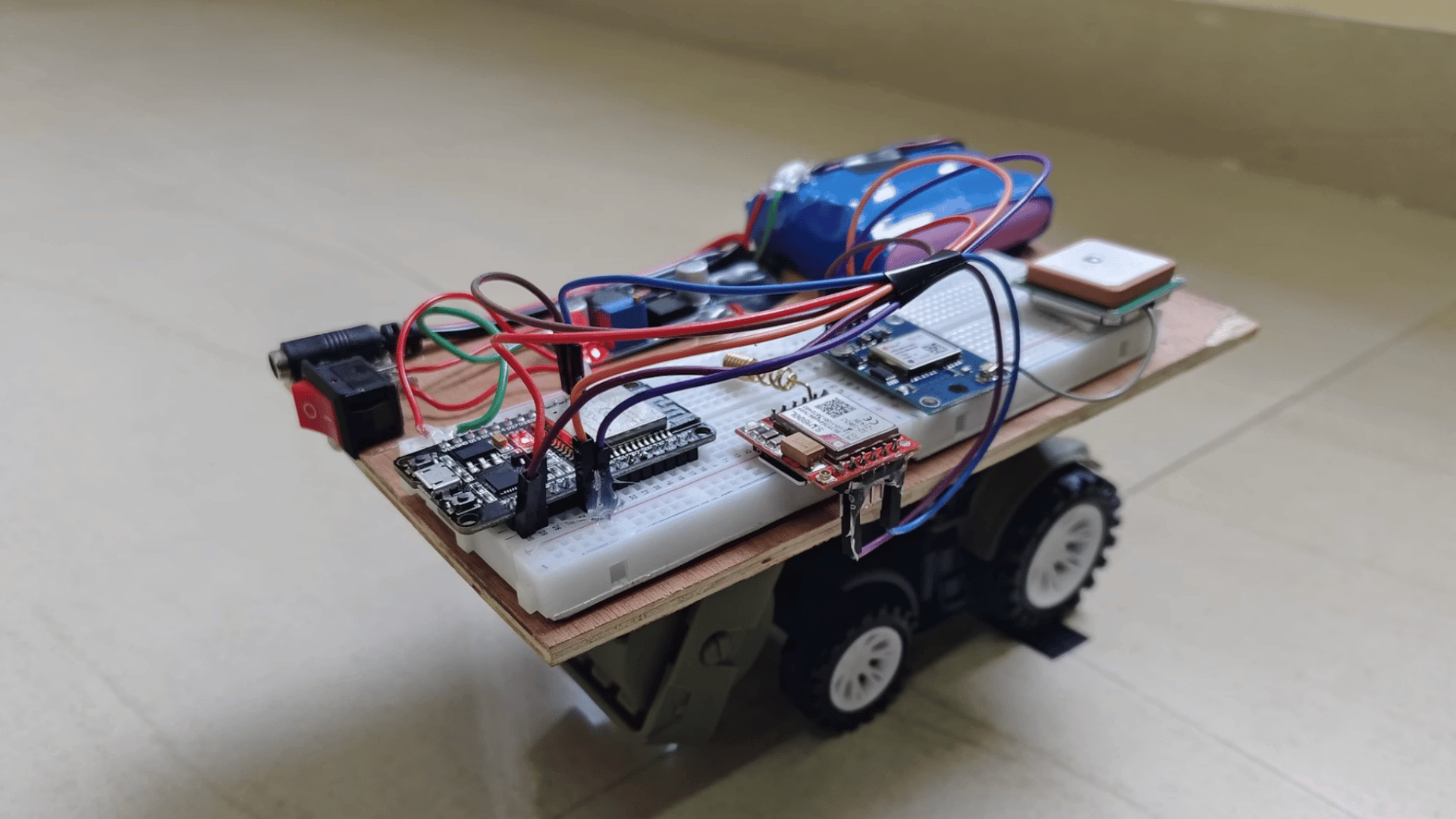 diy wheeled robot with breadboard microcontroller battery pack and connected wires mounted on a wooden platform