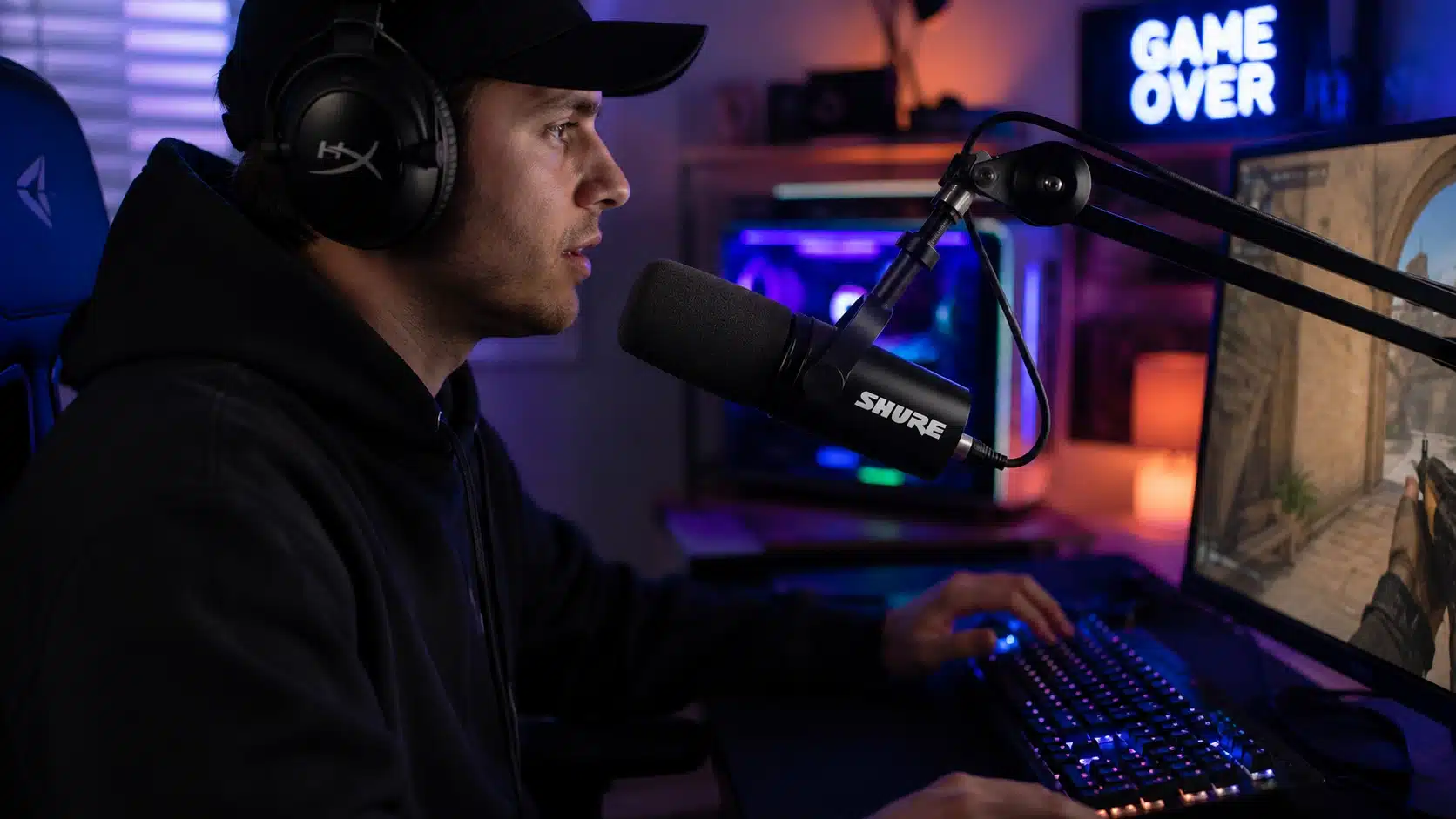 gamer using a shure microphone on boom arm while streaming in an rgb-lit gaming room with desktop setup