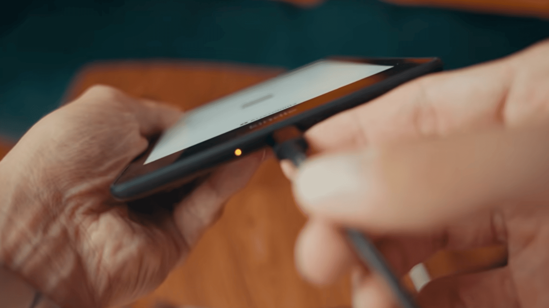 hand connecting a charging cable to the bottom port of a kindle ereader during troubleshooting (1)