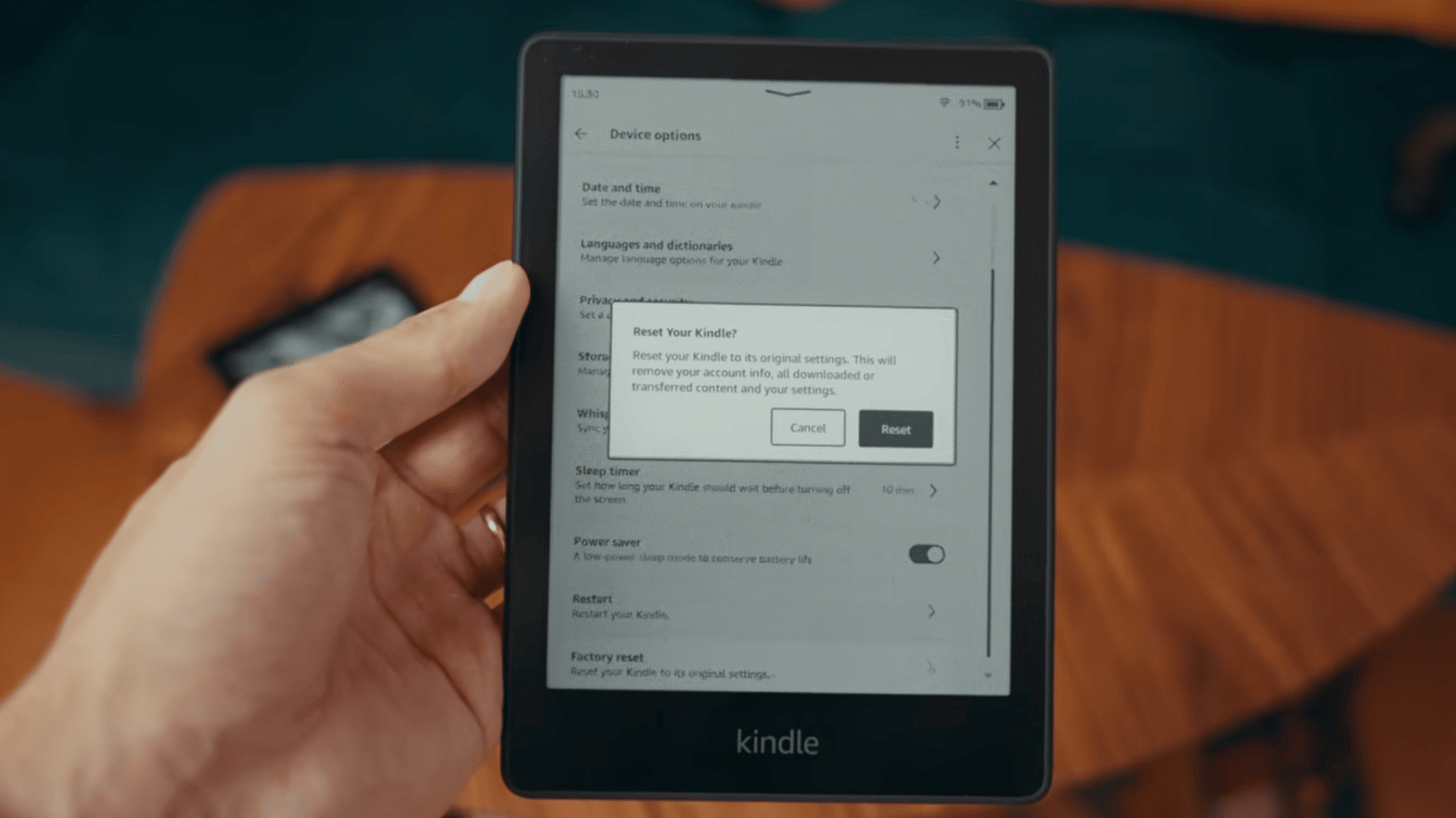 hand holding a kindle ereader displaying a factory reset confirmation message in the device settings menu
