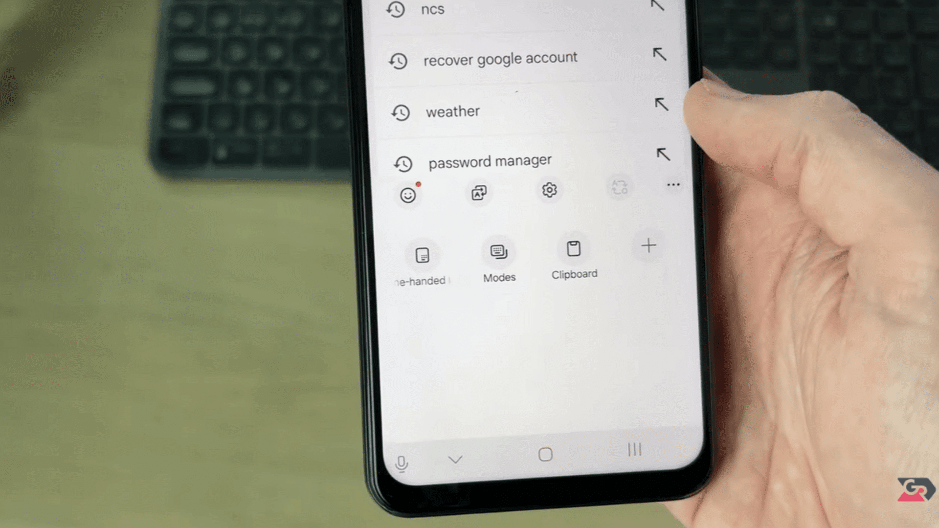 hand holding a smartphone showing keyboard search history and shortcut icons with a desktop keyboard behind