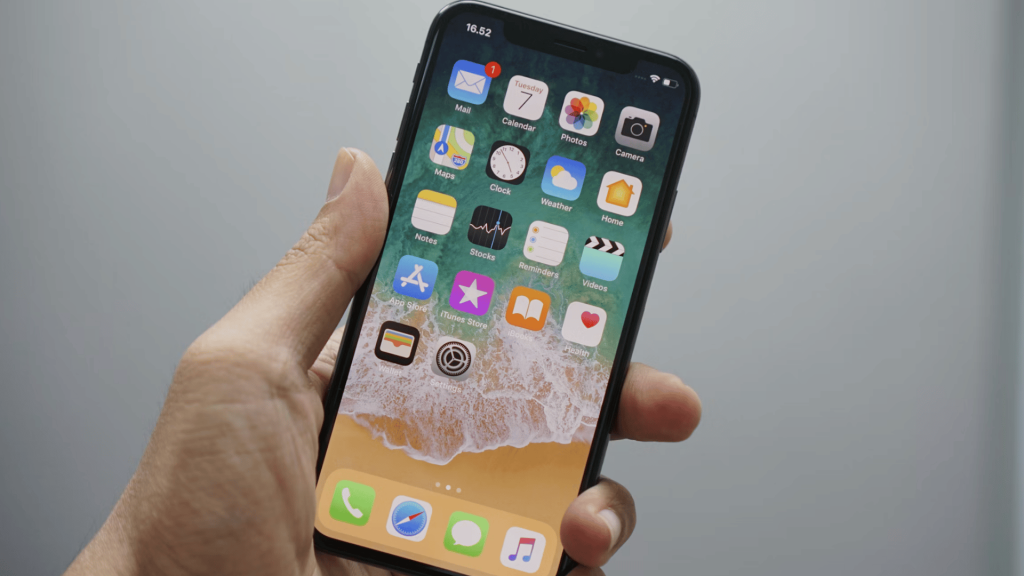 hand holding an iphone displaying the home screen with app icons against a plain light gray background