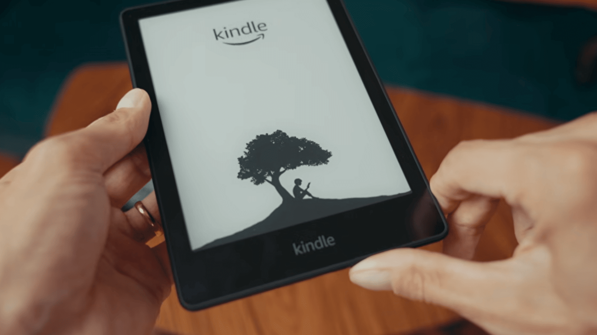 hands holding a kindle ereader displaying the startup screen with the reading logo and tree illustration