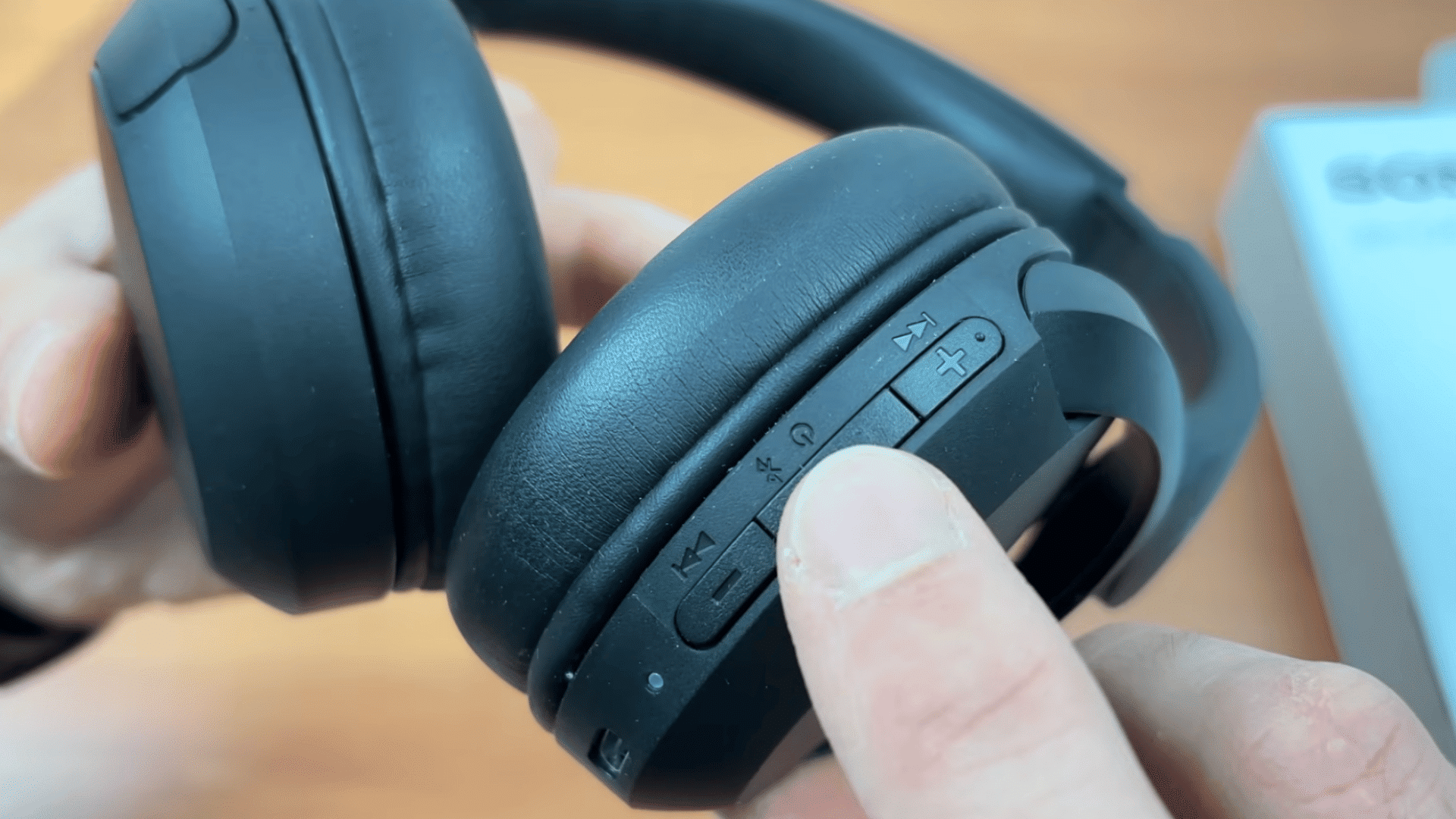 hands holding black over ear headphones while highlighting the usb c charging port and control buttons