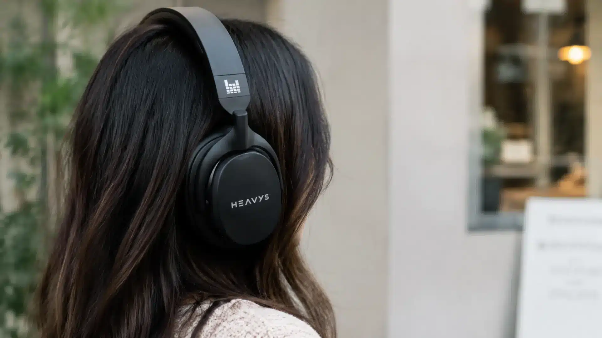 HEAVYS over-ear headphones worn by a woman from the side in a realistic lifestyle café setting
