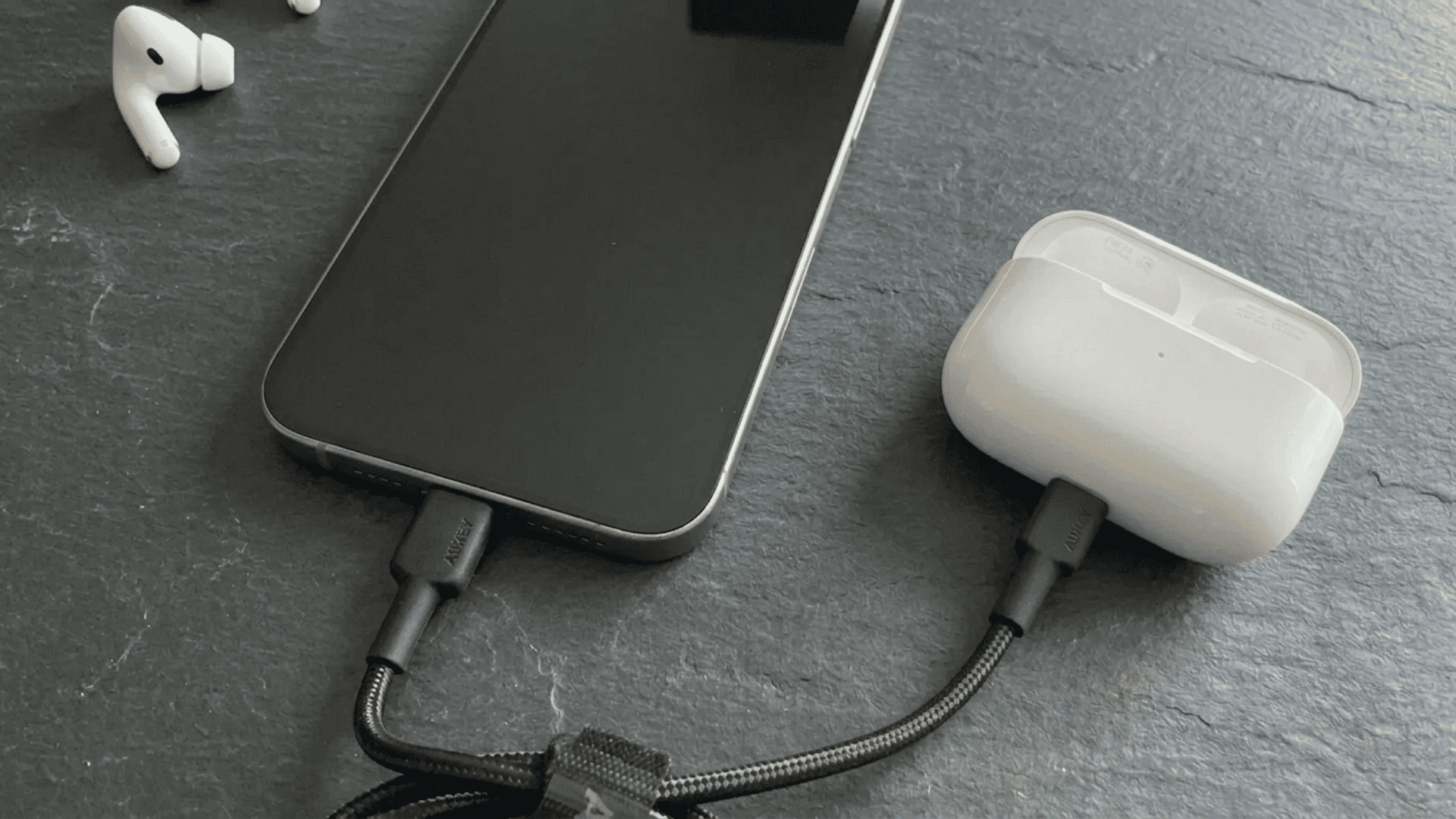 iPhone and AirPods charging with cables on a dark tabletop