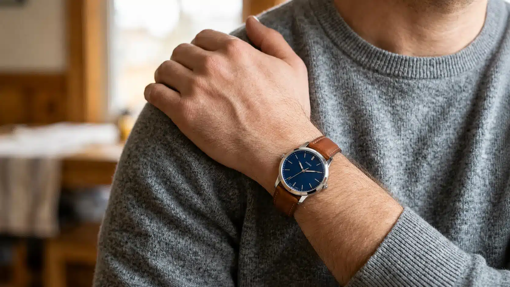 Man wearing a blue dial Fossil watch with brown leather strap while resting hand on shoulder indoors