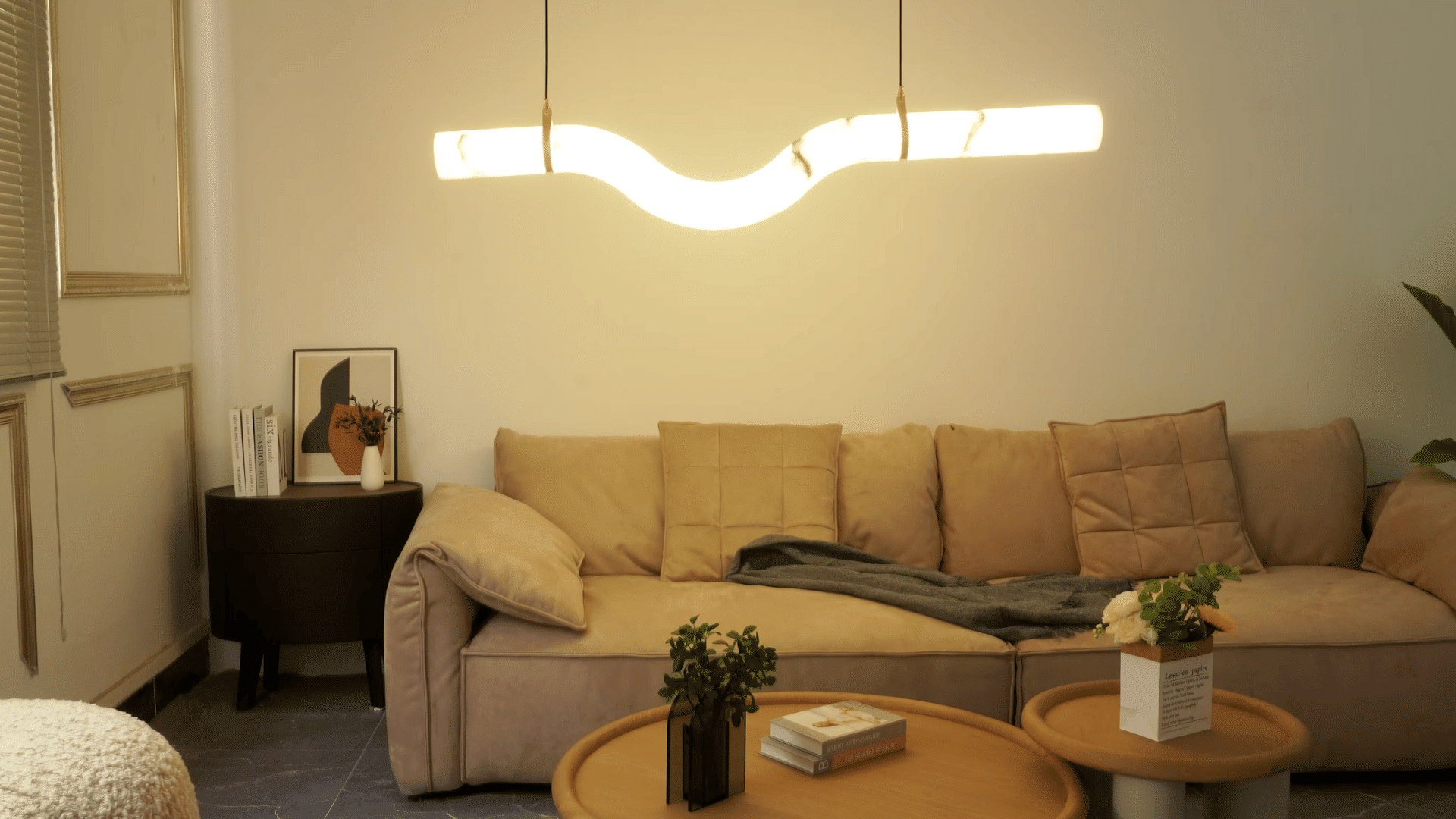 modern living room with a curved pendant light above a beige sofa and wooden coffee tables with plants and decor