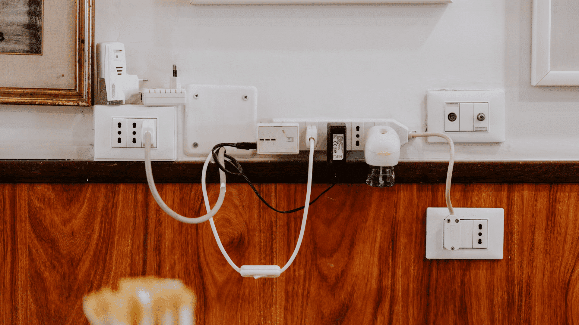 multiple wall outlets with connected chargers adapters and cables mounted above a wooden wall panel indoors