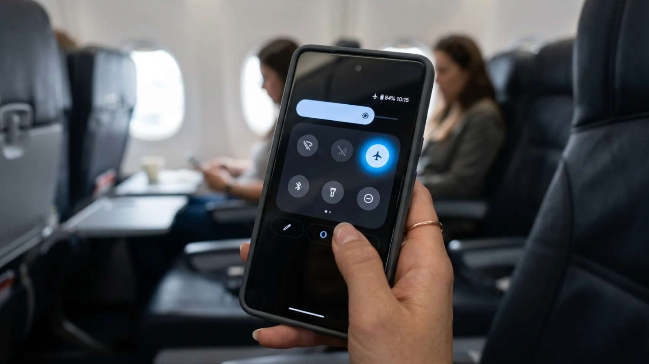 person enabling airplane mode on smartphone during flight while seated inside commercial aircraft cabin before takeoff safely