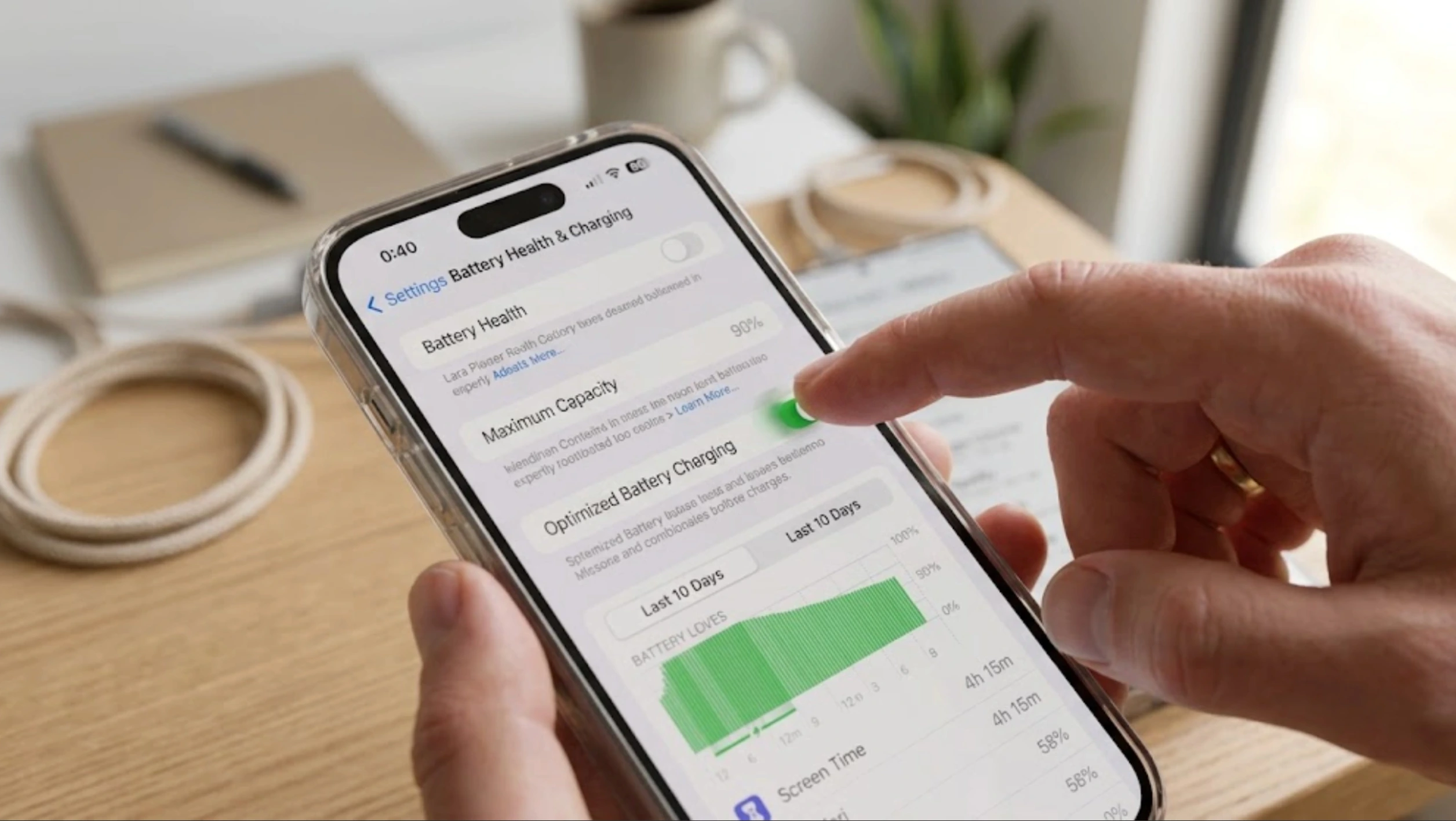 person enabling optimized battery charging on a smartphone while viewing battery health settings at a tidy workspace
