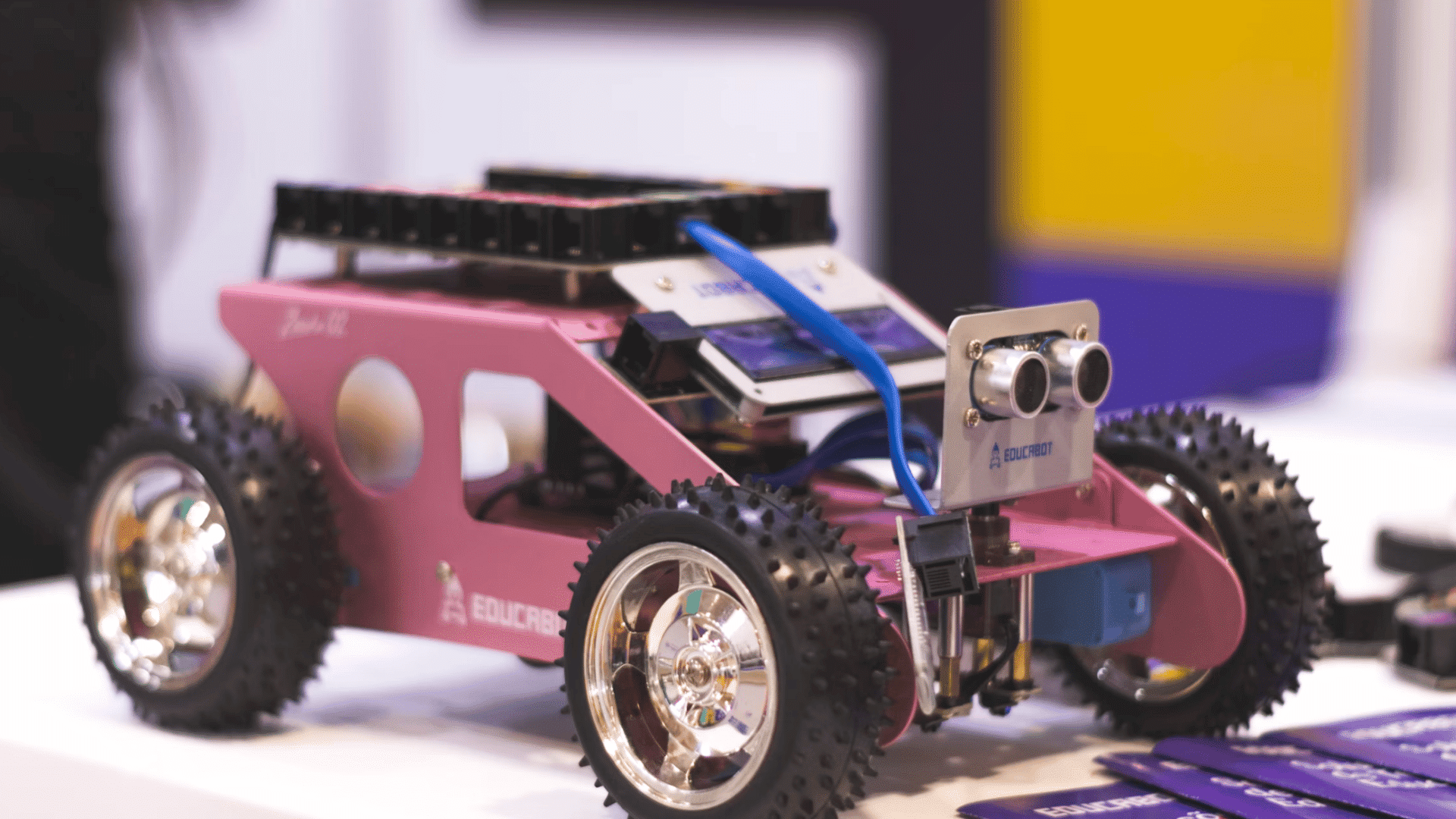 pink robotic car with ultrasonic sensor module mounted on a metal chassis displayed on a tabletop