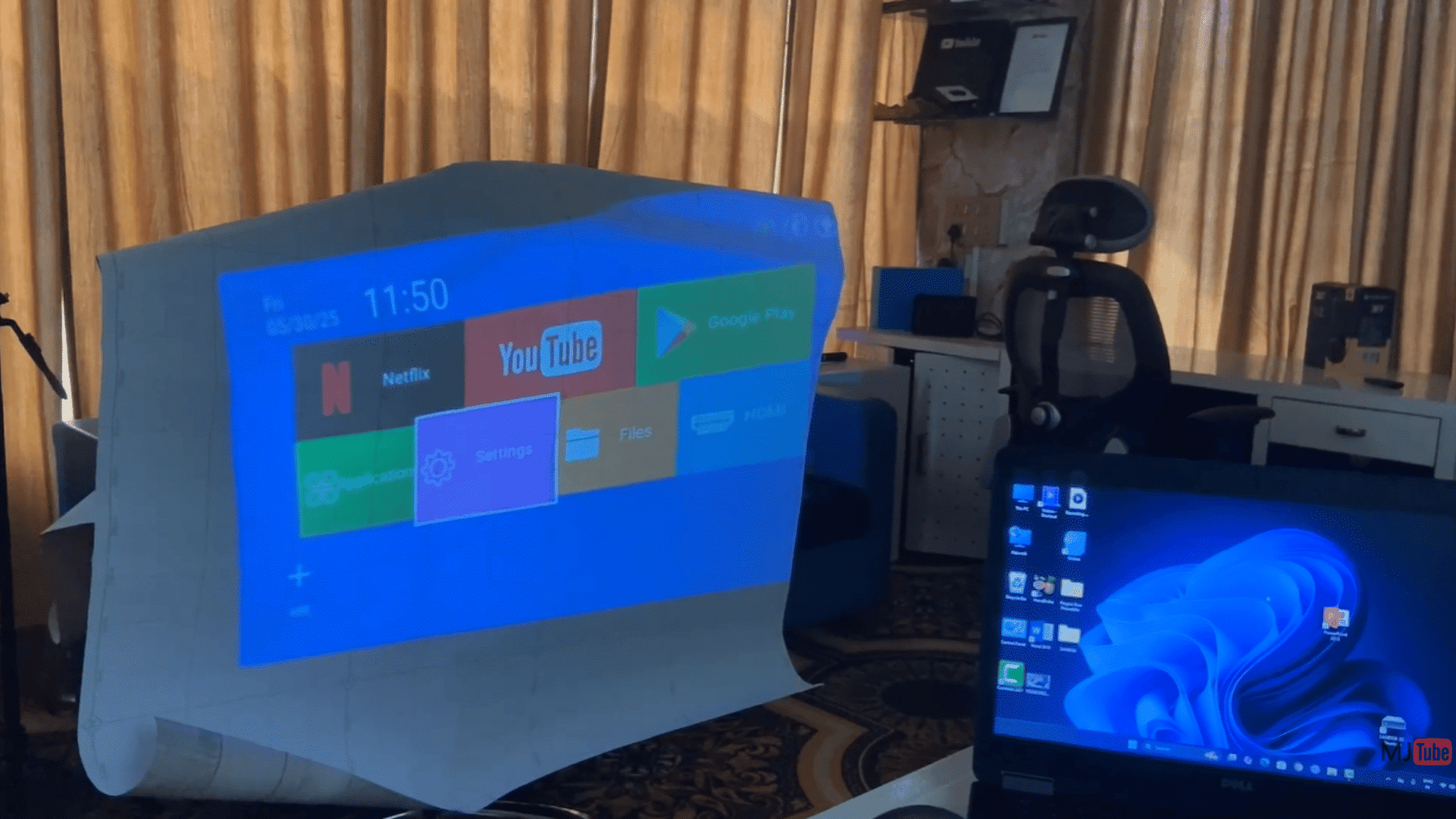 projector displaying a smart tv interface on a fabric screen beside a laptop in an indoor office workspace