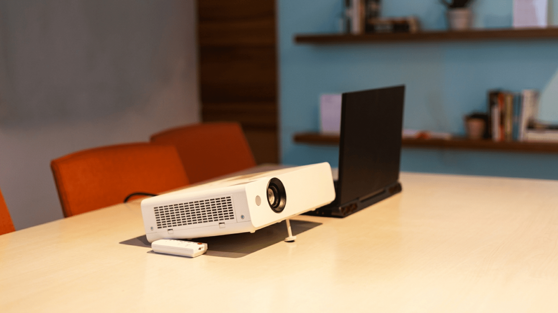 projector with a remote beside an open laptop on a conference table in a modern meeting room