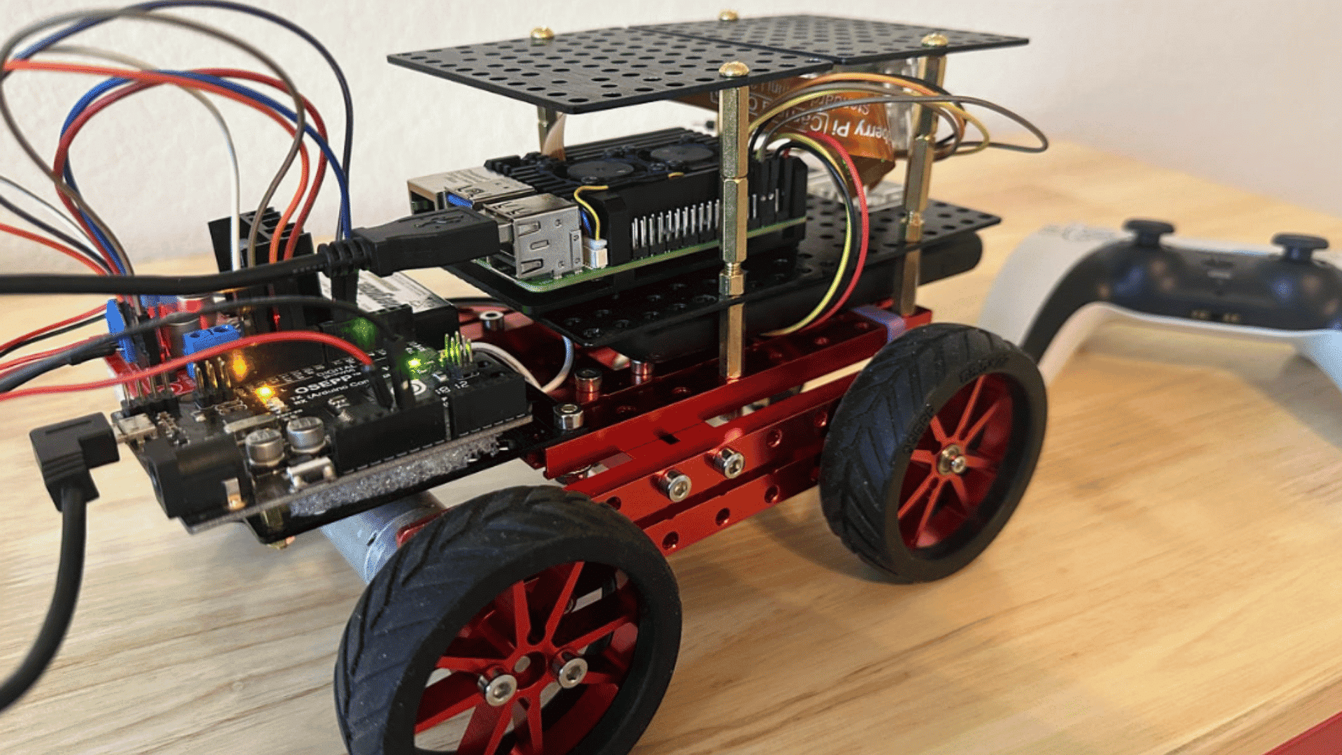 raspberry pi powered robot car with stacked electronics large wheels and connected controller on a wooden desk