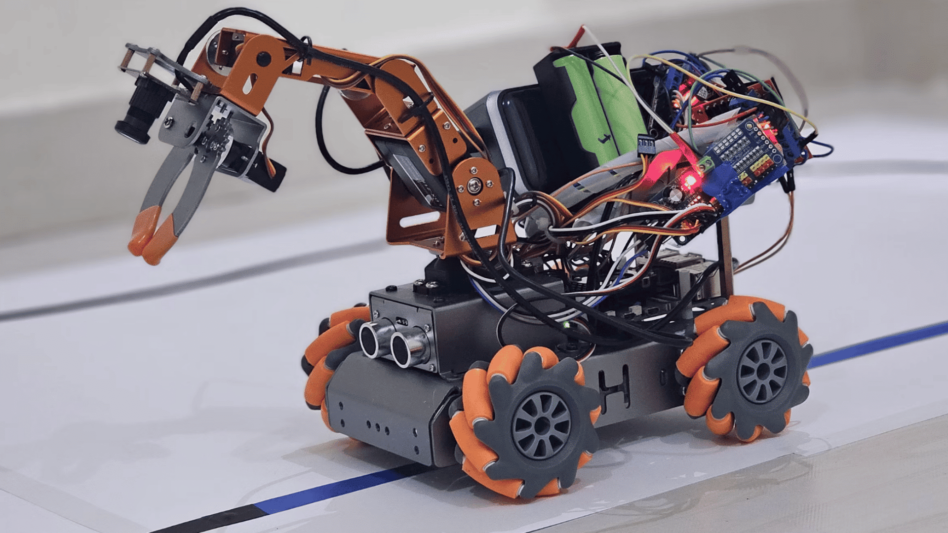 robotic vehicle with a mechanical gripper arm sensors exposed electronics and omni wheels on a test surface