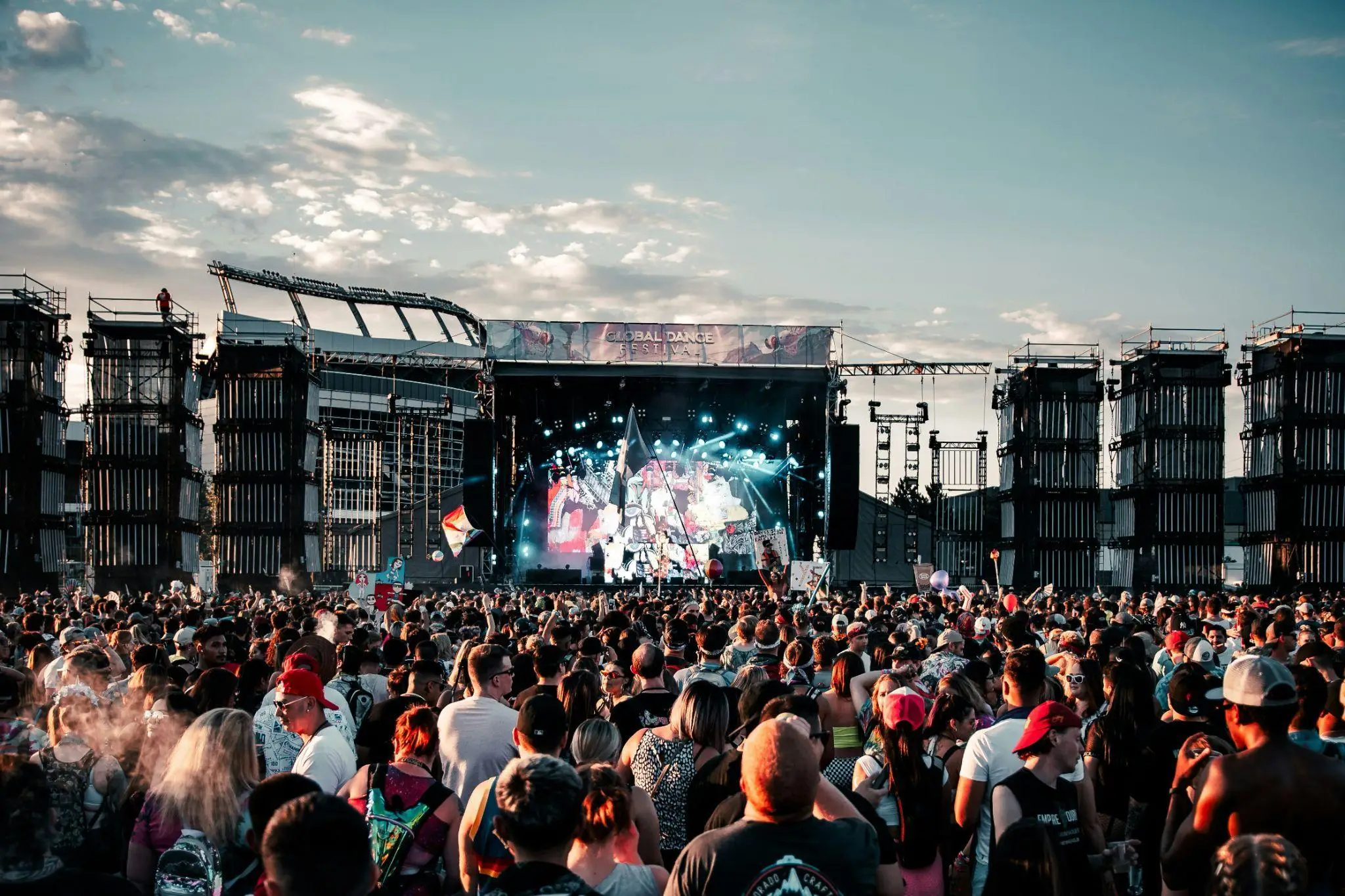 Crowd gathered at large outdoor music festival in front of illuminated stage under clear sky
