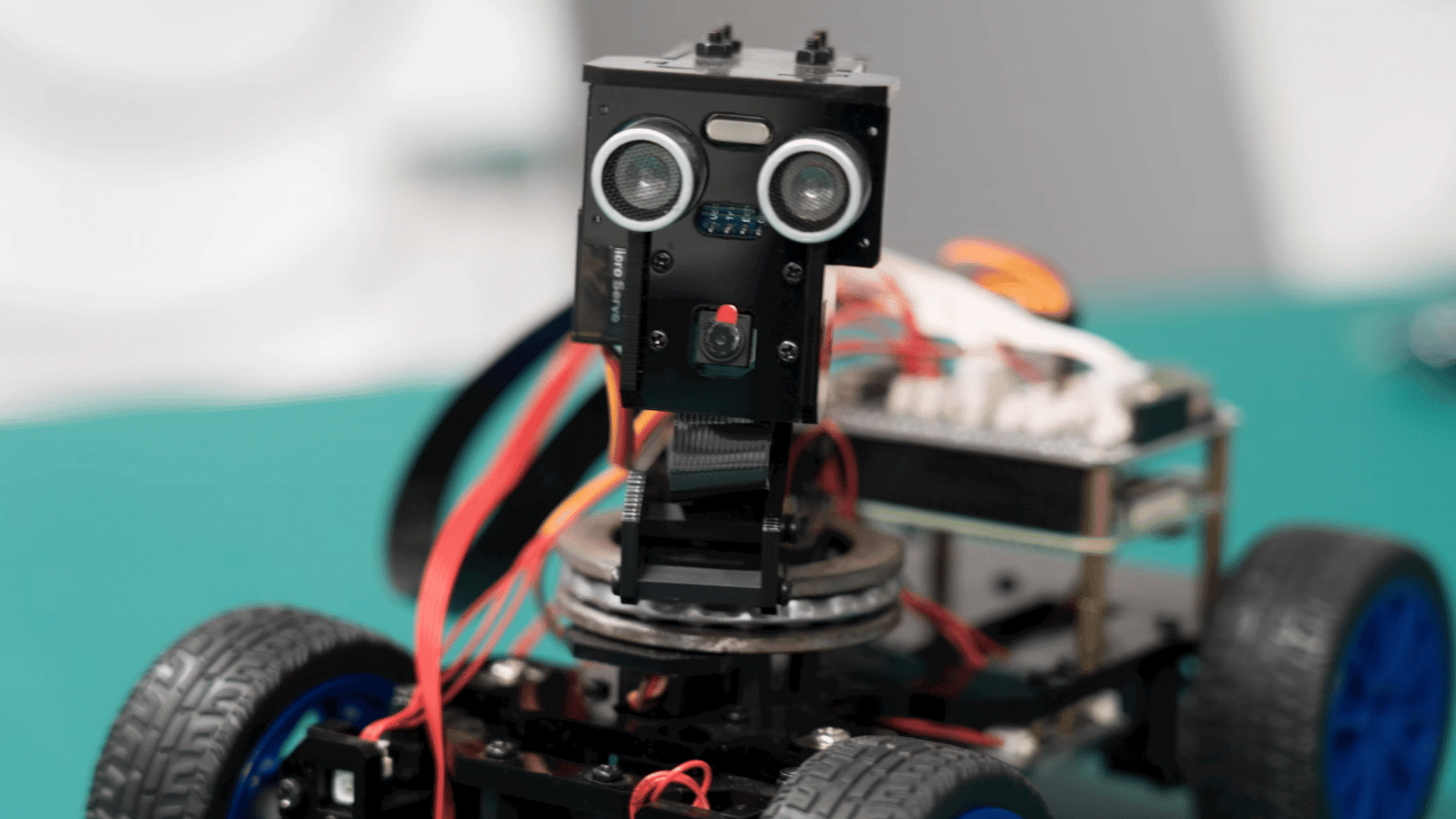 small robot car with ultrasonic sensors camera module and exposed wiring mounted on a four wheel chassis