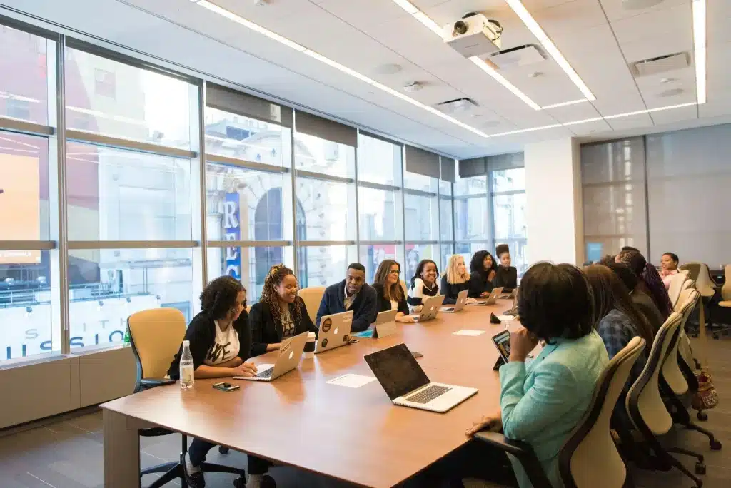 People working on laptops around large conference table in modern office with large windows