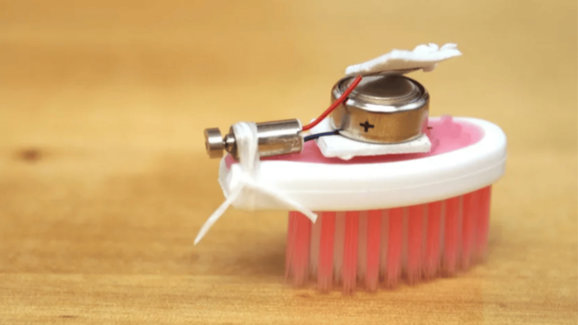 tiny vibrating brush robot with a coin battery small motor and toothbrush base on a wooden surface