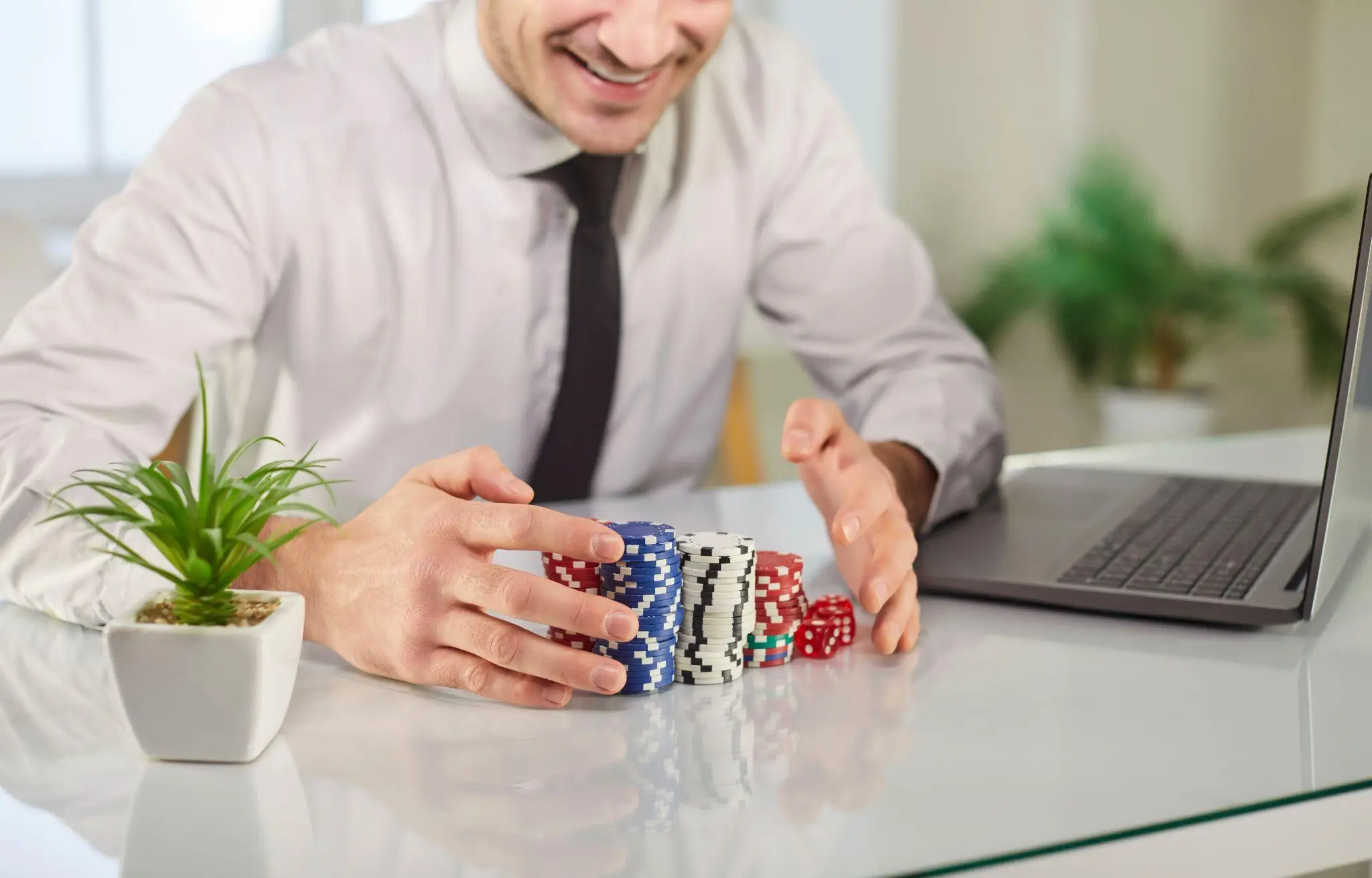 Man stacking poker chips at desk with laptop and small plant nearby