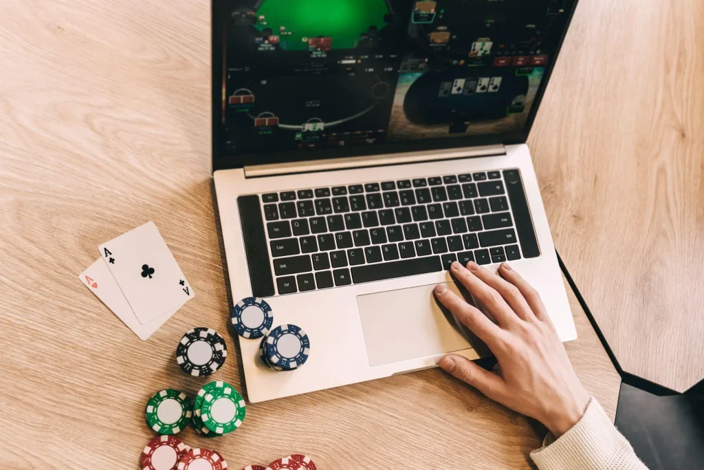 Poker game on laptop with chips and cards on wooden table