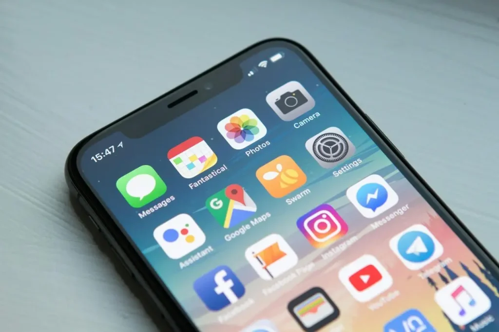 Smartphone screen displaying various apps on a light wooden surface