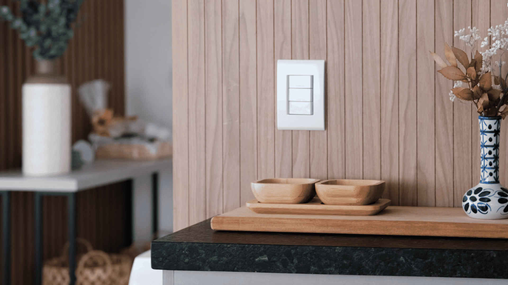 white light switch mounted on a wood paneled wall above a counter with wooden bowls and a decorative flower vase