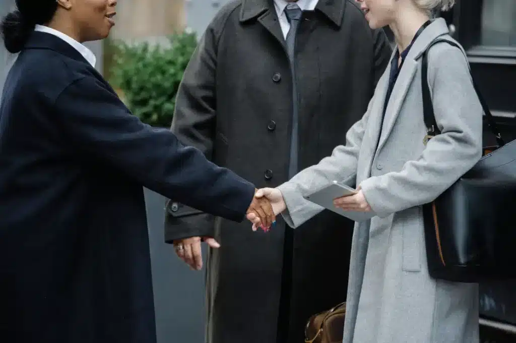 Business professionals in dark coats shaking hands outdoors with another holding a tablet