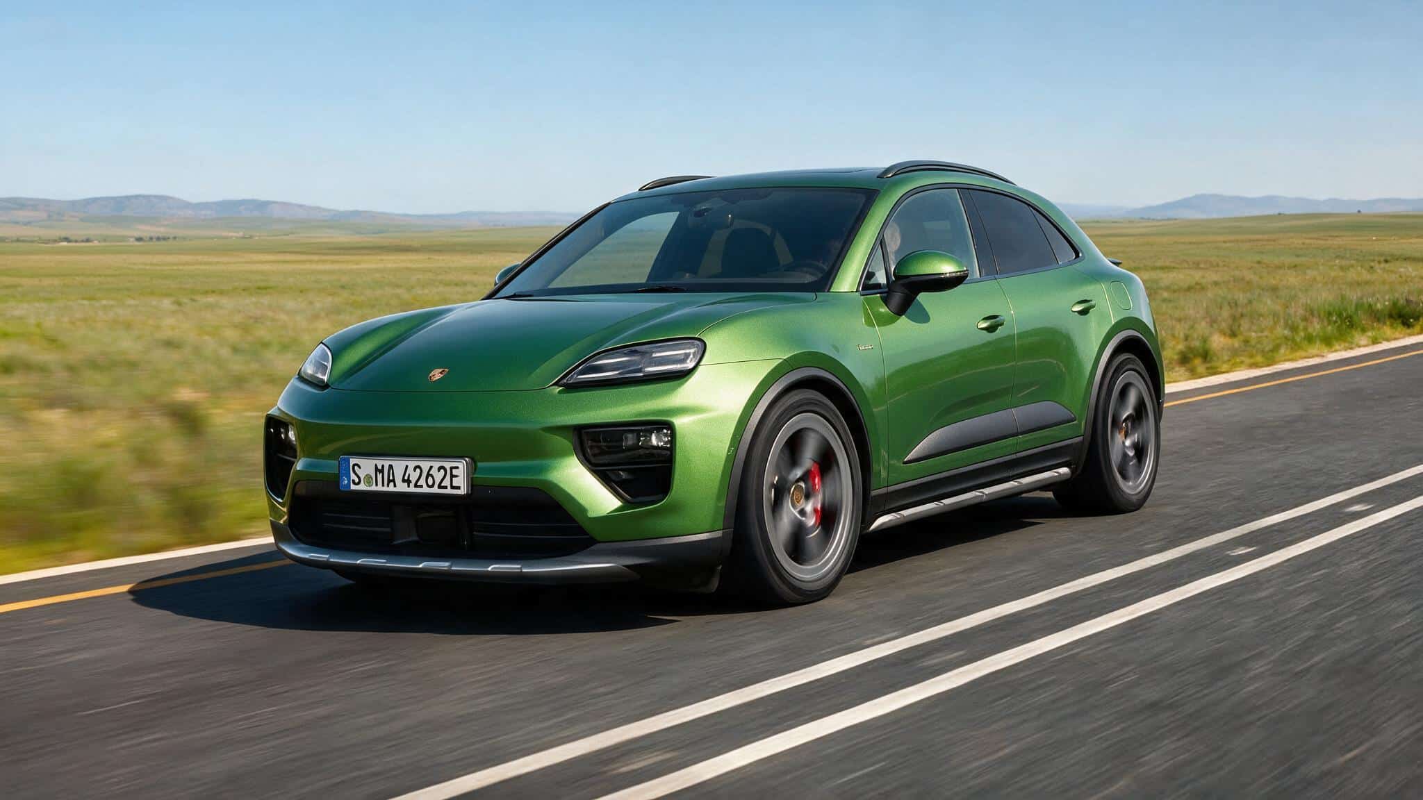 green porsche macan electric suv on open highway through grassland with distant hills sleek curved body and alloy wheels