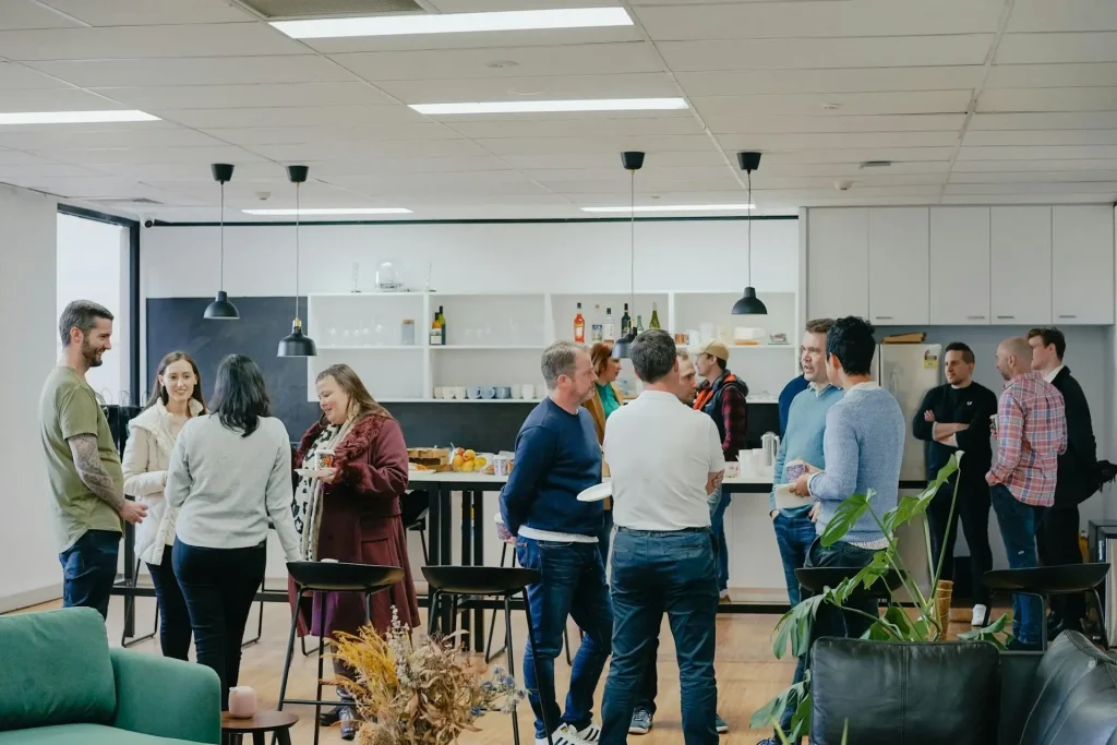 People socializing in a modern office kitchen with hanging lights and plants