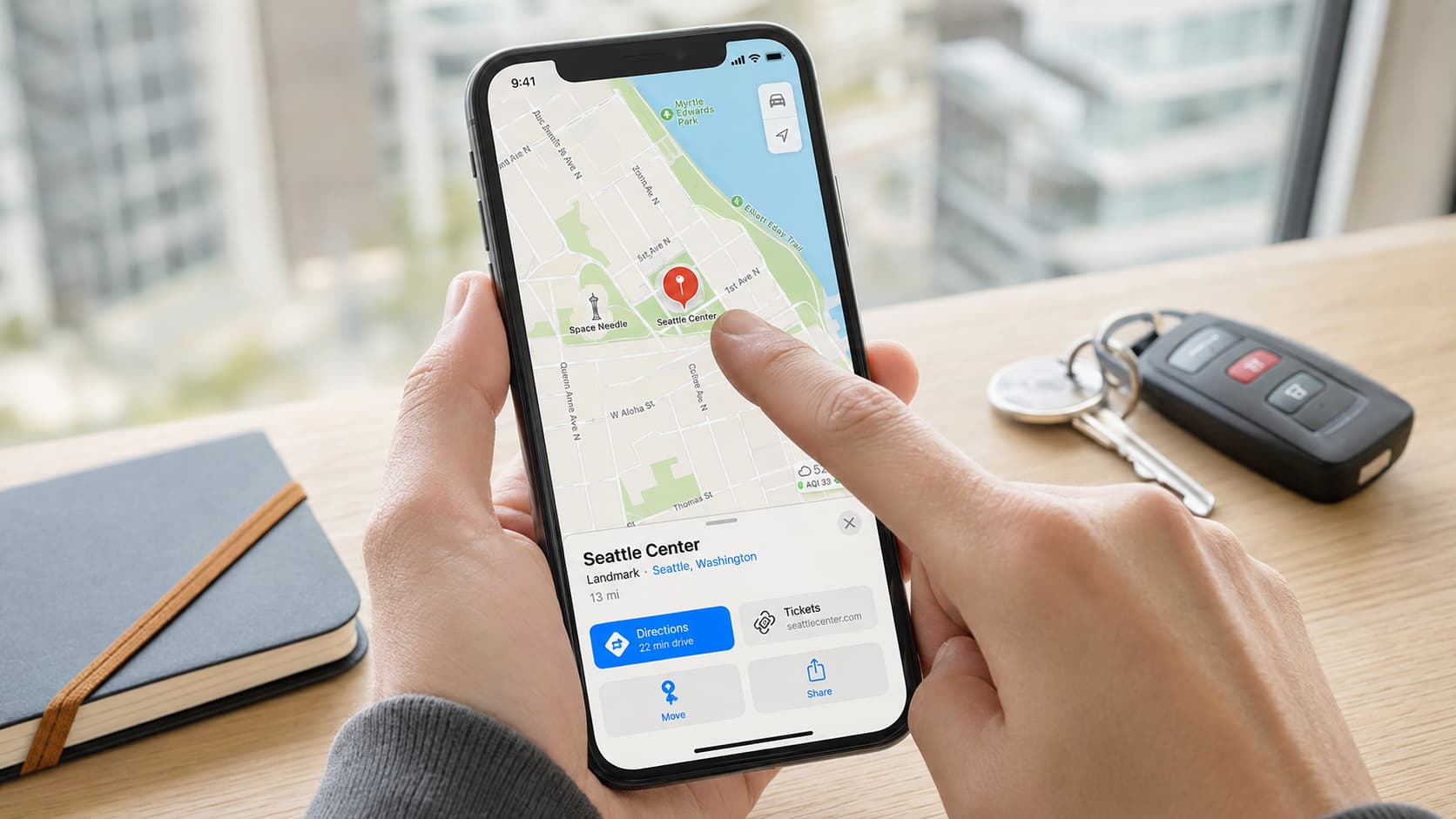 person dropping a red location pin in apple maps on an iphone beside car keys and a travel notebook