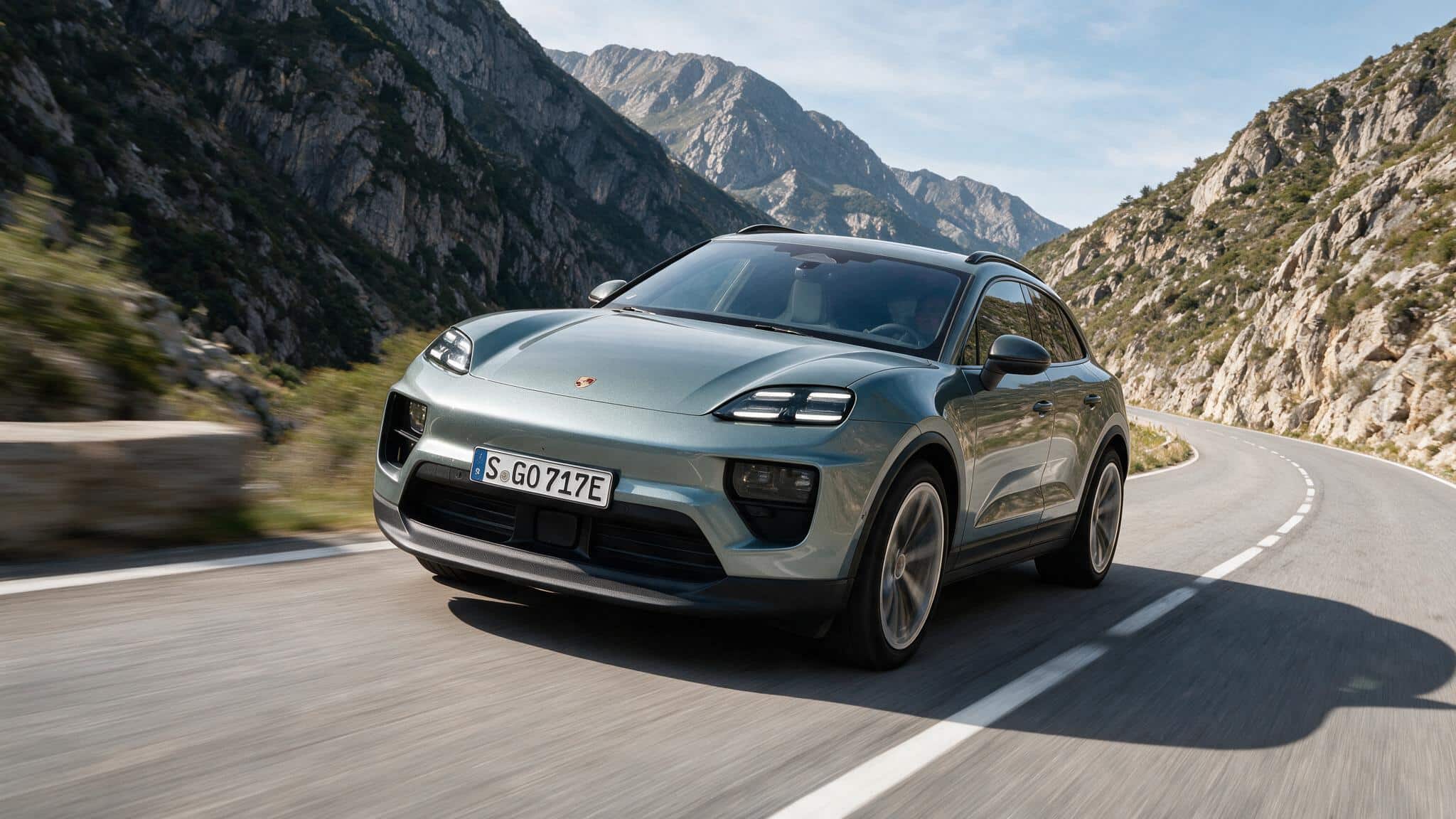silver porsche macan electric suv on winding mountain road with rocky cliffs sleek silhouette alloy wheels led lights